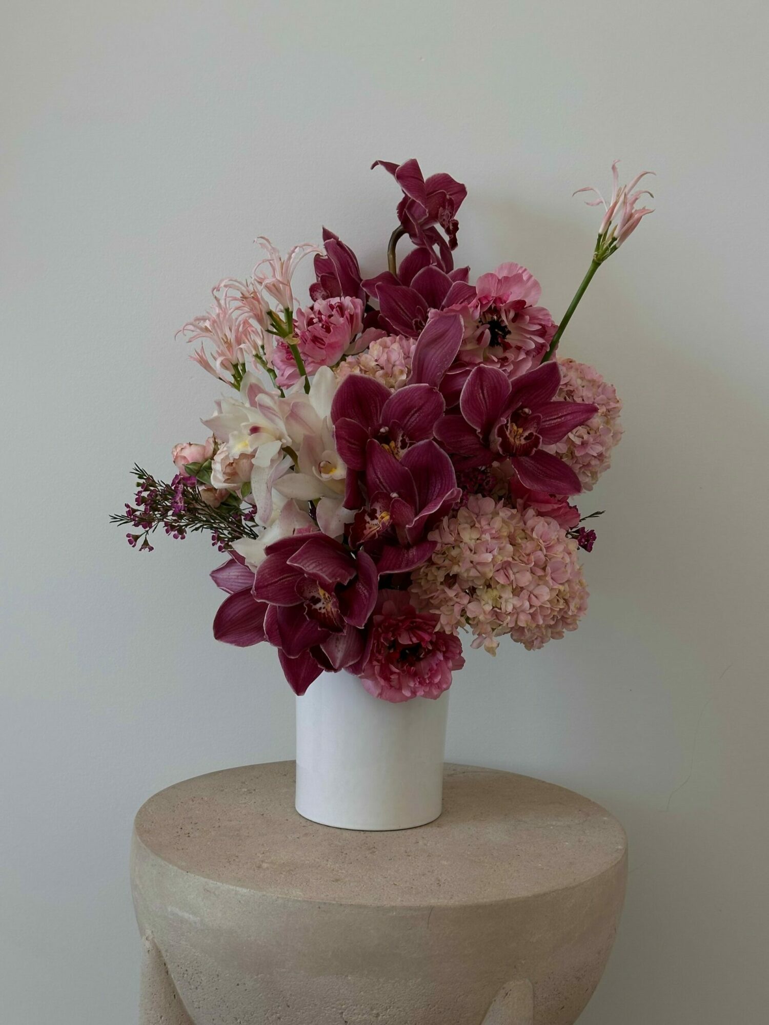 Flower arrangement with pink and purple flowers in a white vase on a round beige table.