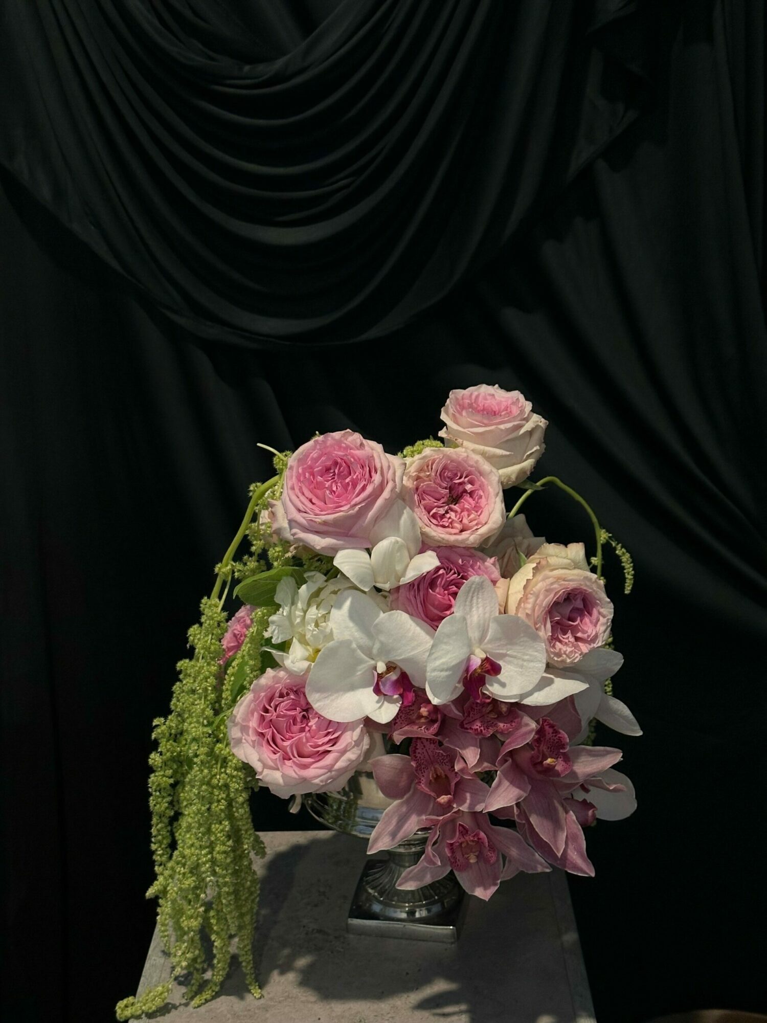 Bouquet of pink and white flowers, including roses and orchids, against a dark background.