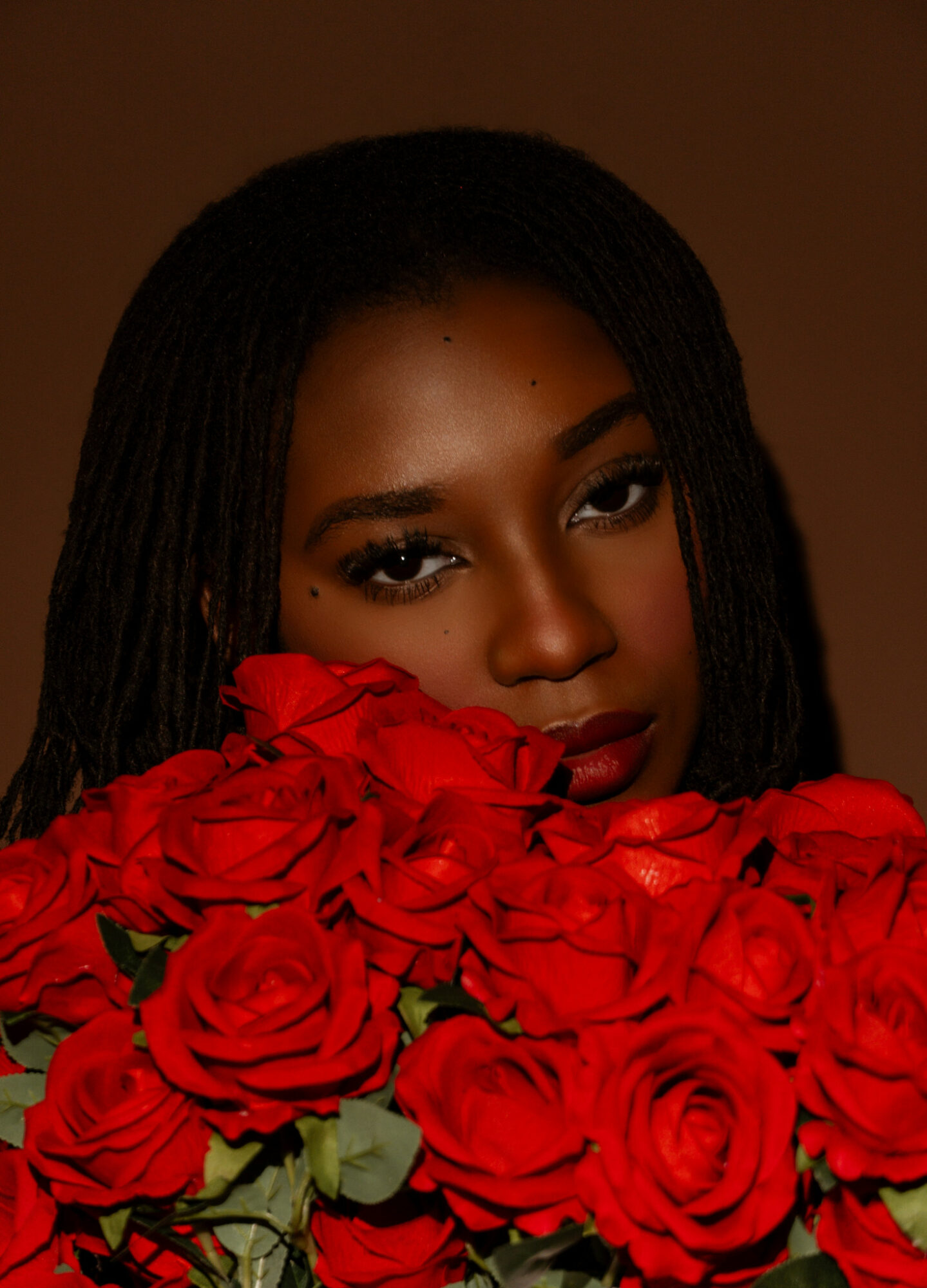 Woman with dark hair and makeup partially obscured by a large bouquet of red roses.