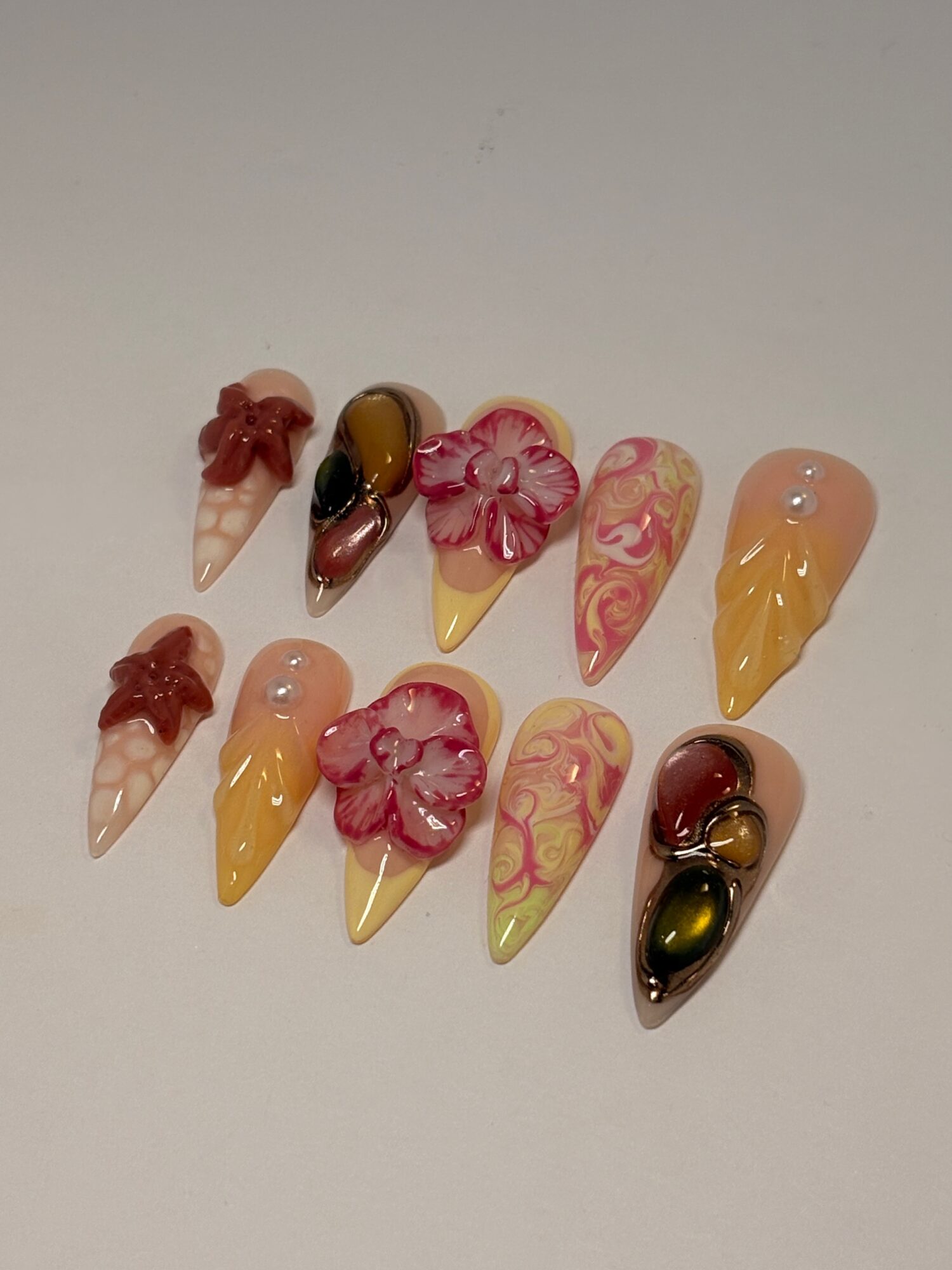 Collection of decorative artificial nails with floral and abstract designs in pink, yellow, and black colors.