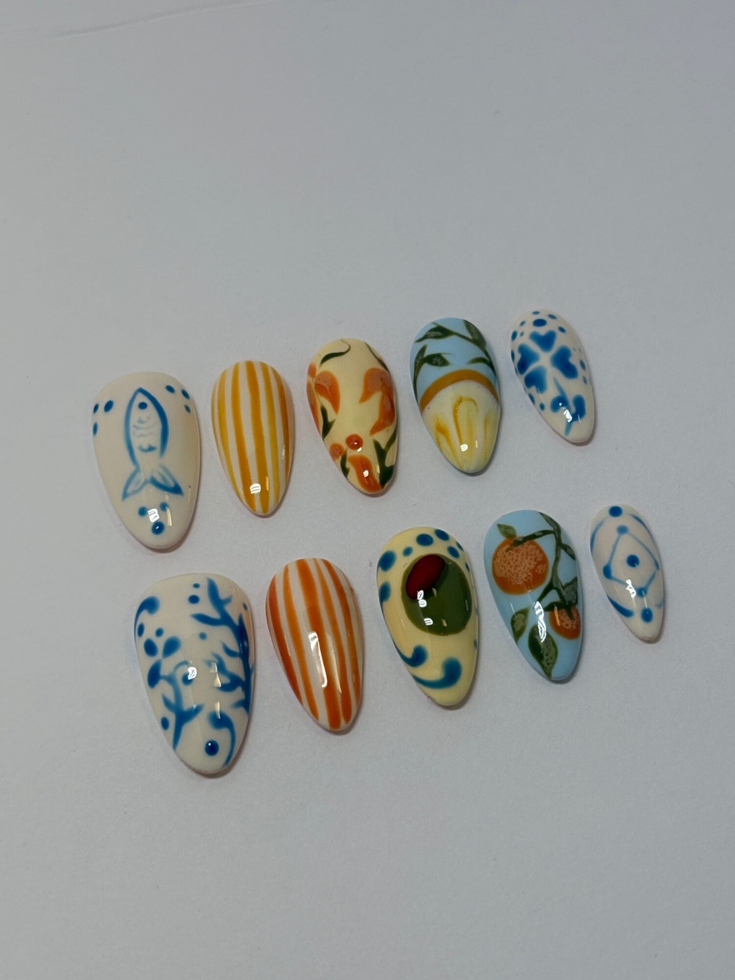 Ten decorated nail tips with colorful patterns, including stripes, floral, and abstract designs, arranged in two rows on a white background.