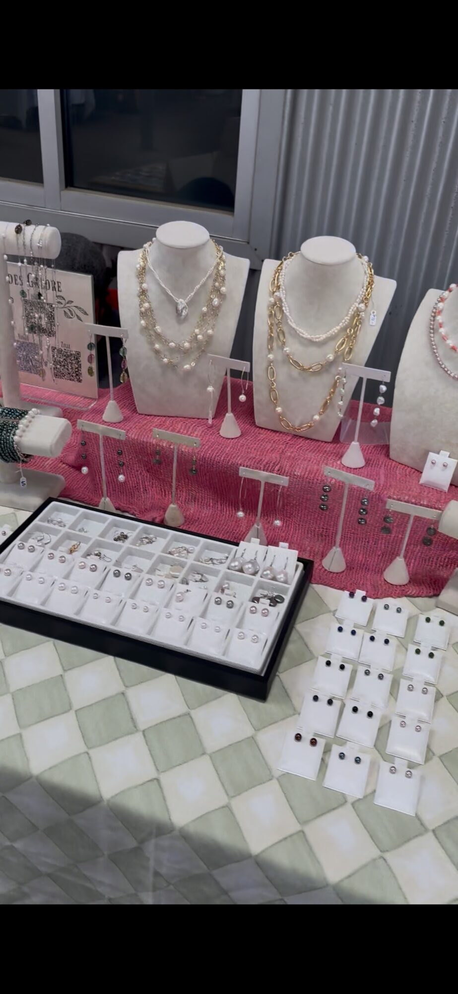 Display of layered pearl necklaces on white busts, jewelry on pink and white surfaces, with a window in the background.