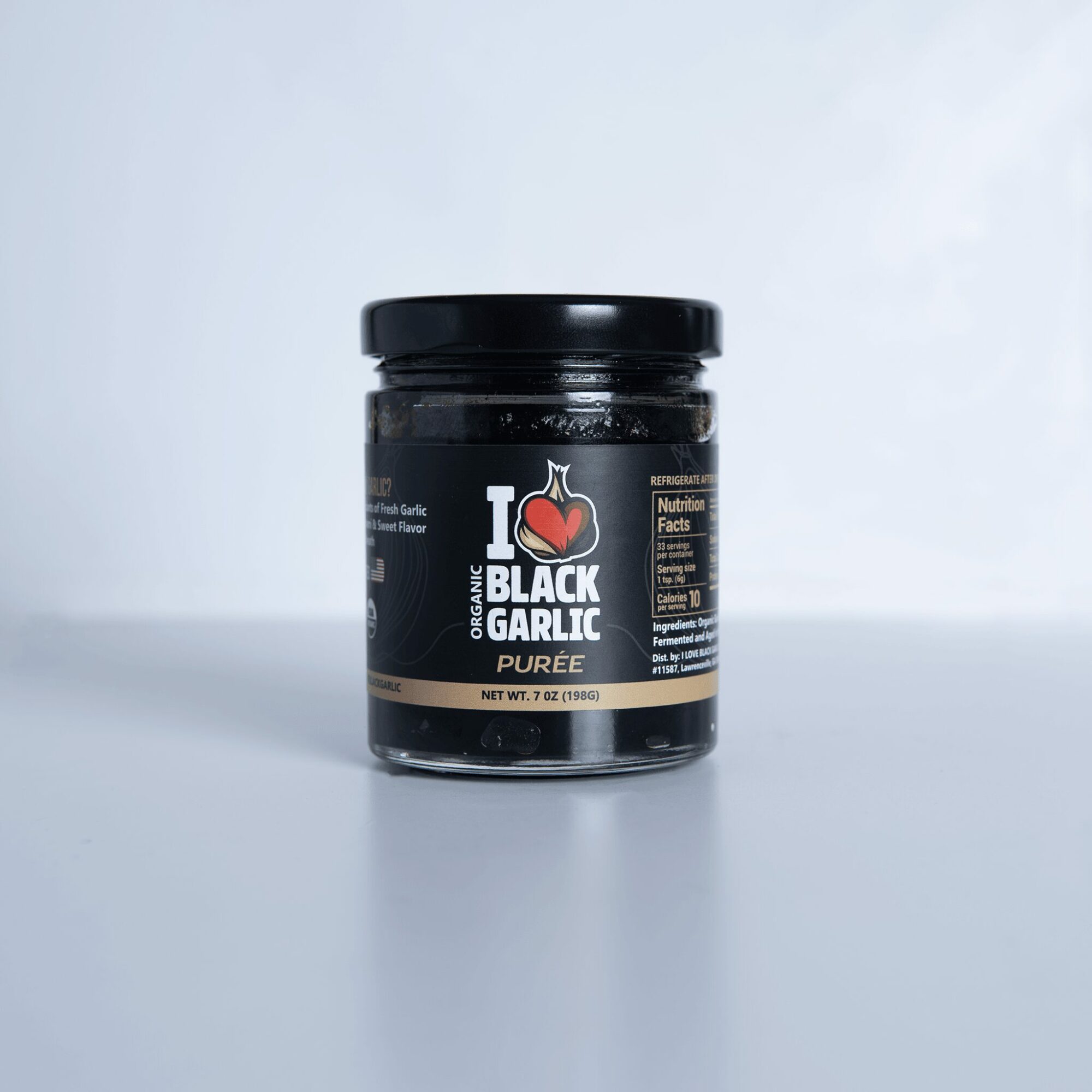A jar of black garlic puree on a light background, label visible with text and logo.