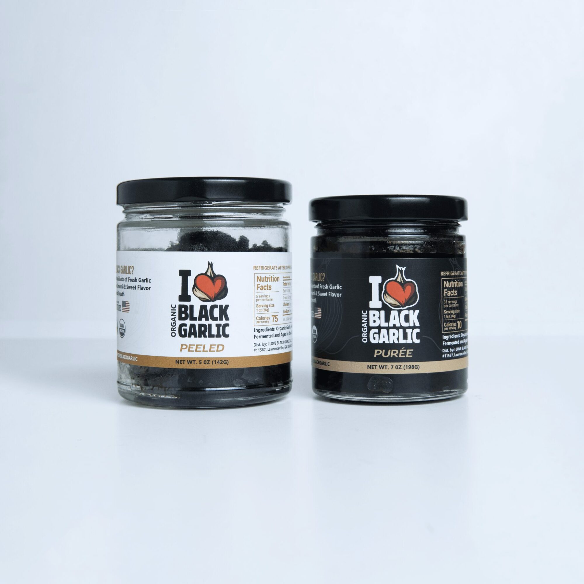 Two jars of black garlic, one peeled and one pureed, placed side by side on a white background.