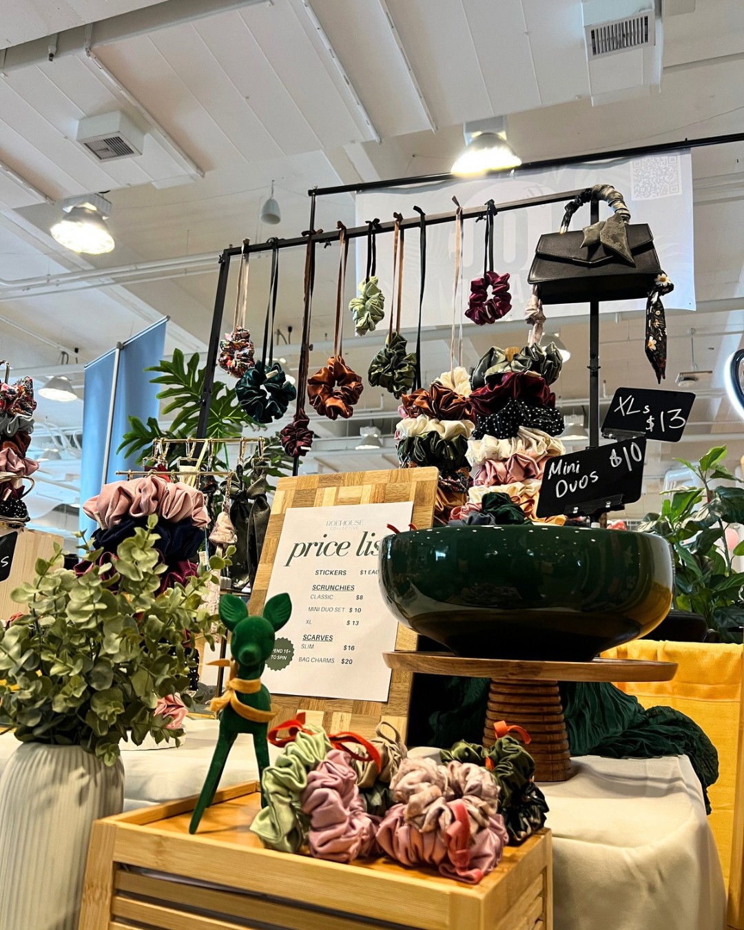 Display of decorative flowers, plants, and accessories on tables and hanging from a black rod in a store interior.