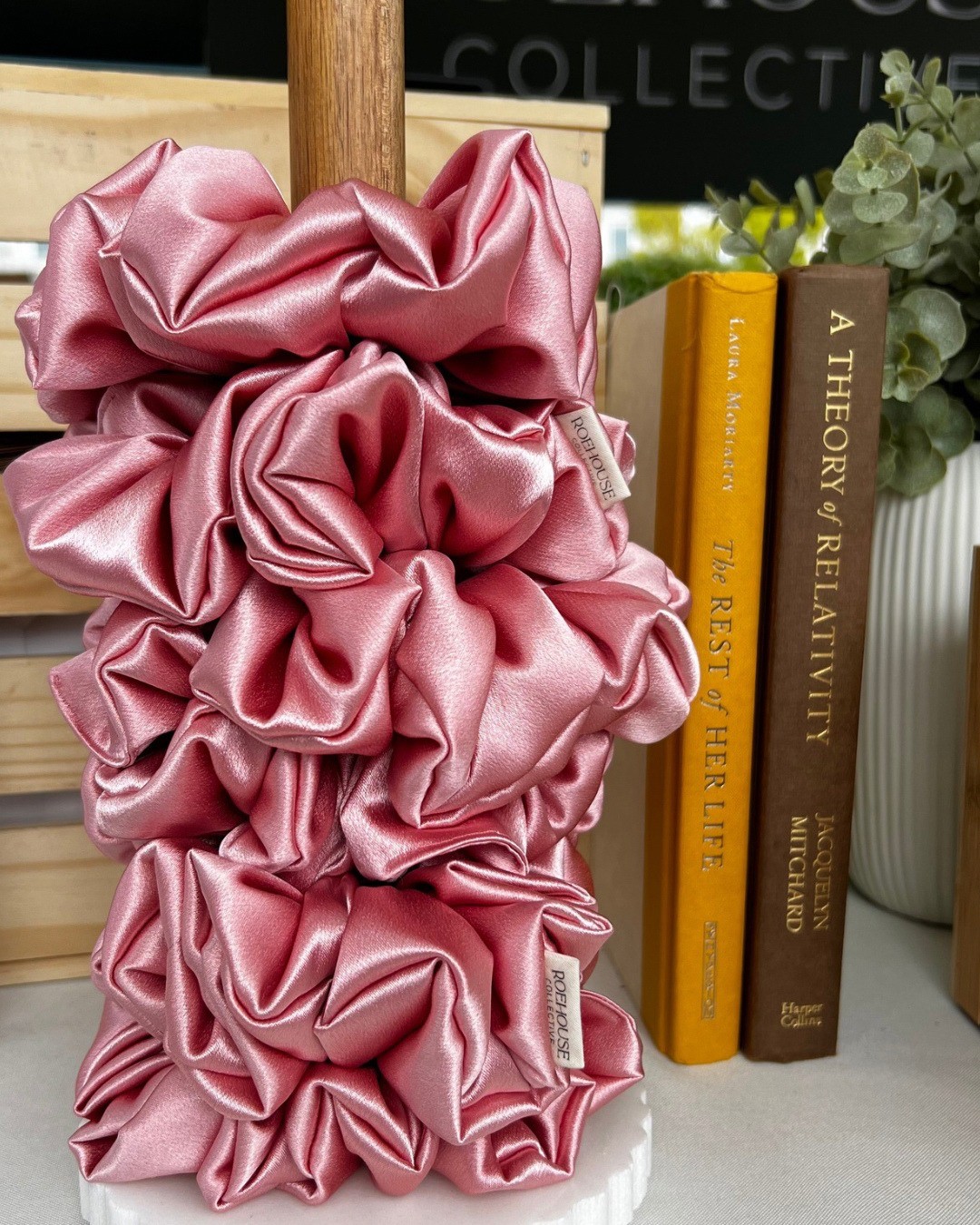 Pink ruffled fabric decoration next to books and a plant on a shelf.