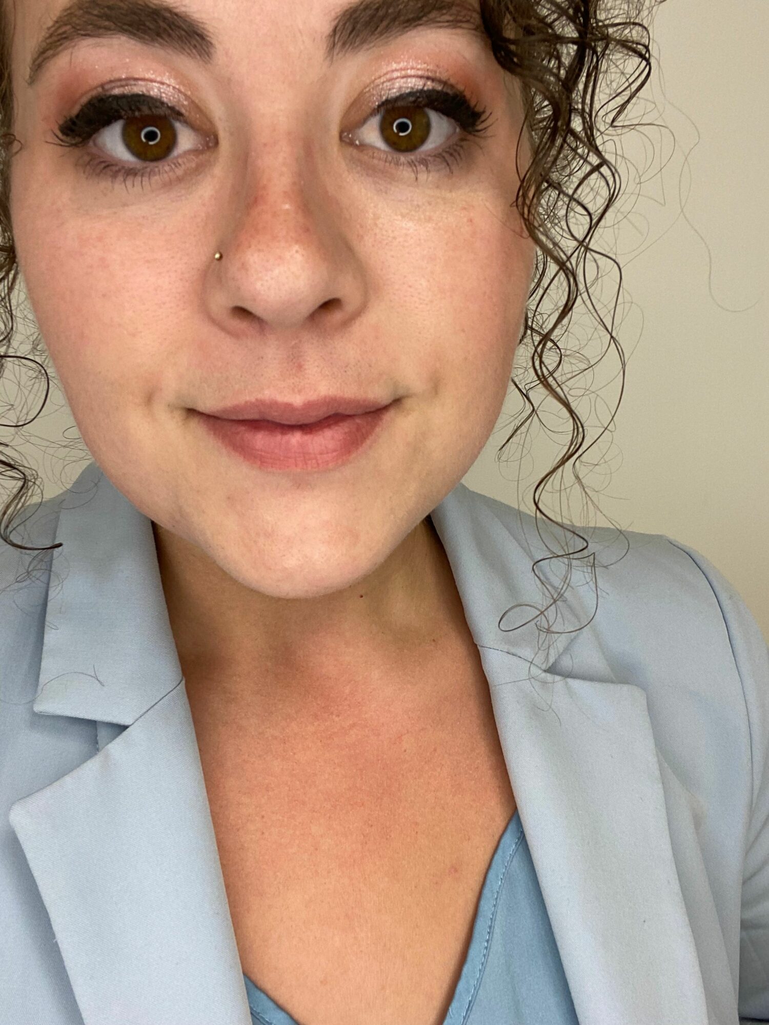 Close-up of a woman with curly hair, wearing a light blue shirt, looking at the camera with a neutral expression.