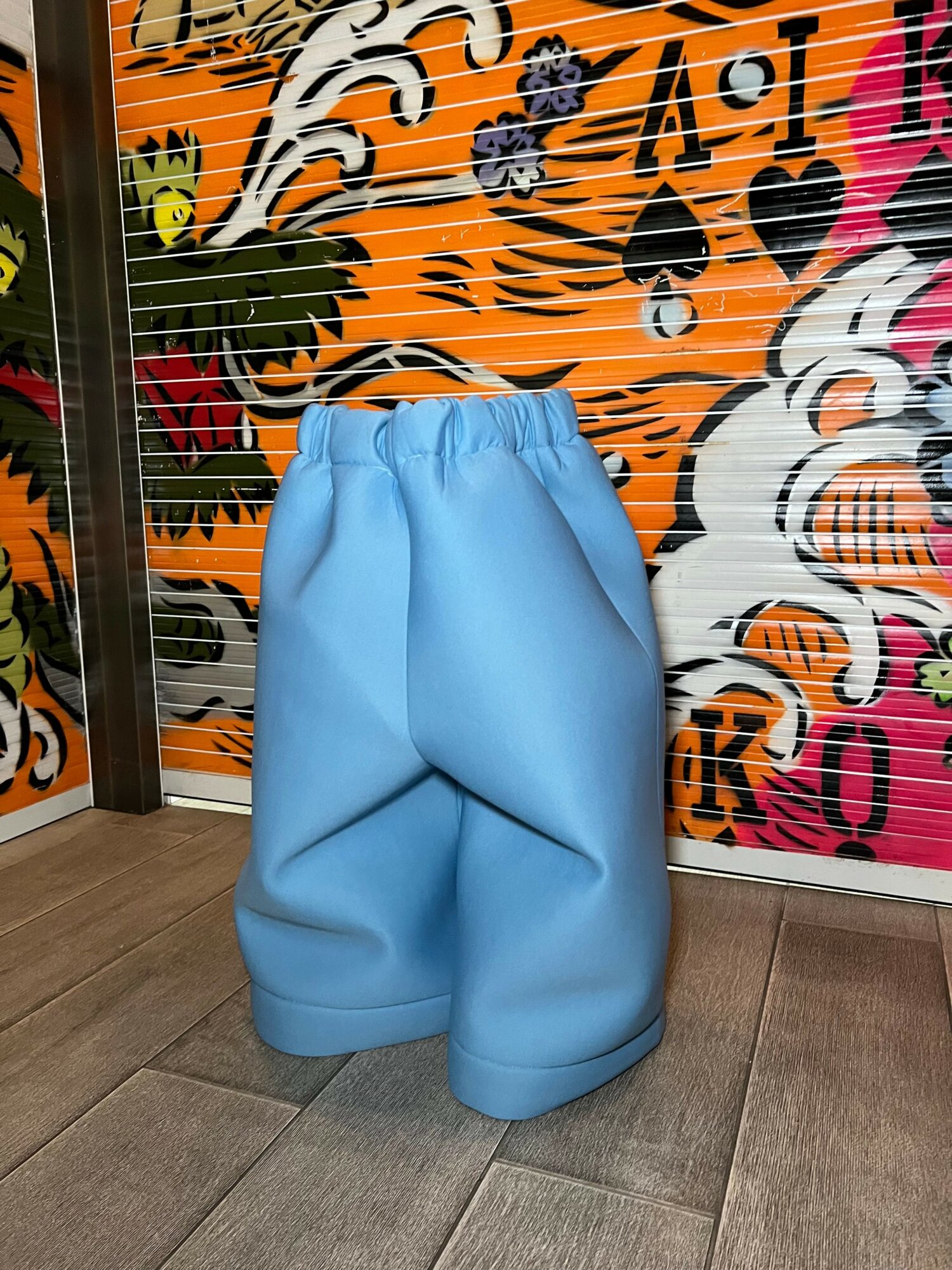 Blue puffy bag or cushion on wooden floor with colorful floral background, viewed from the side.