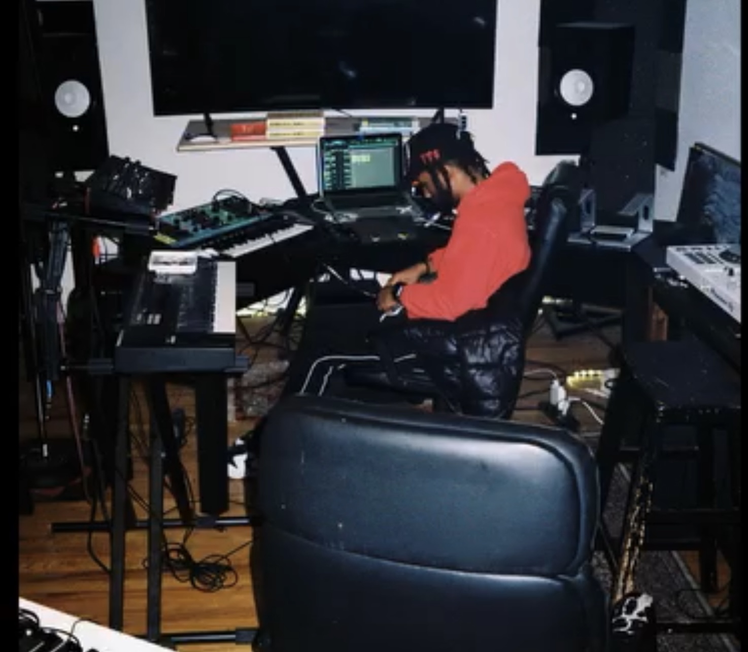 Person with dreadlocks in a red hoodie working with music equipment in a studio.