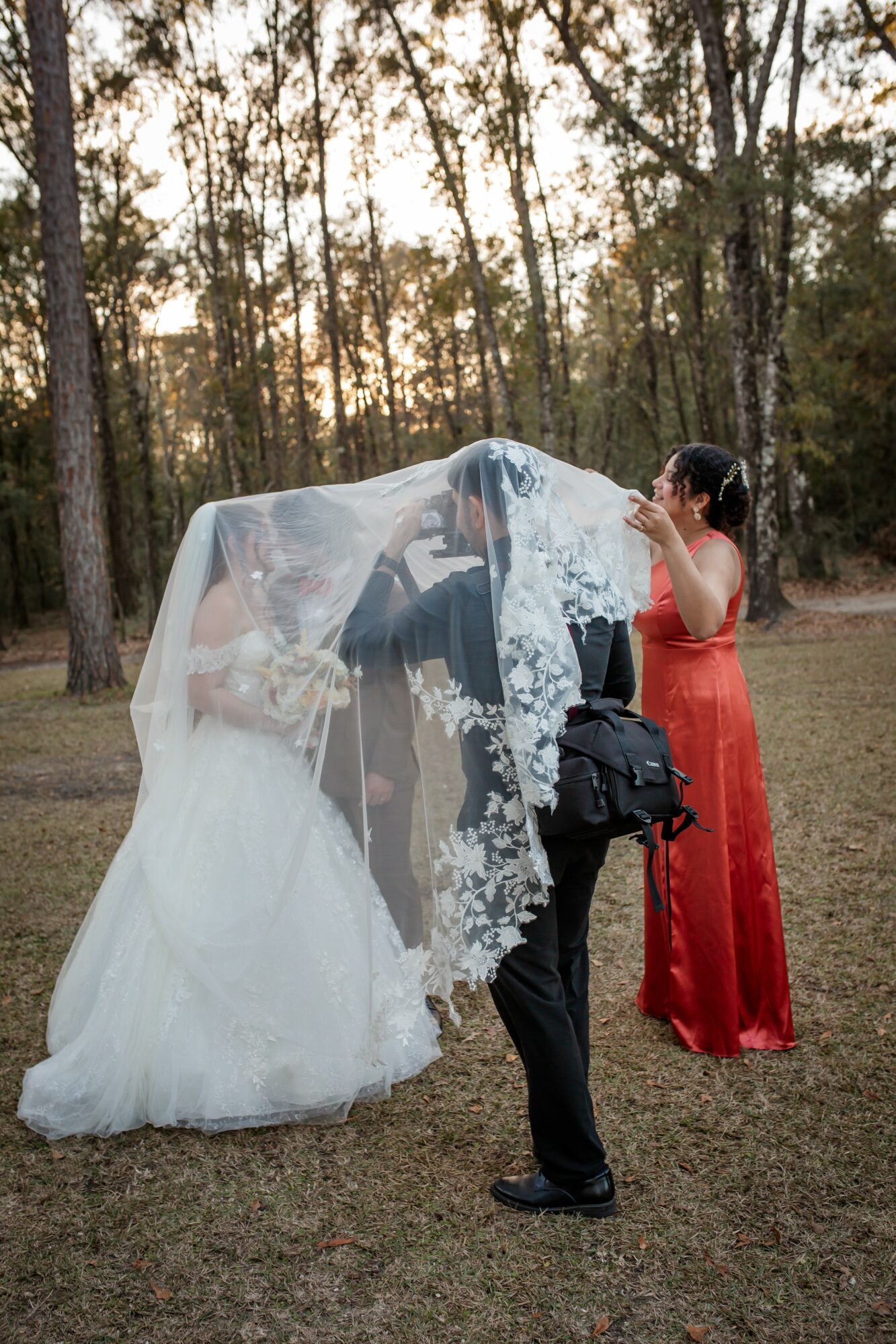 Person in wedding dress and another in red dress under a veil in a forest setting.