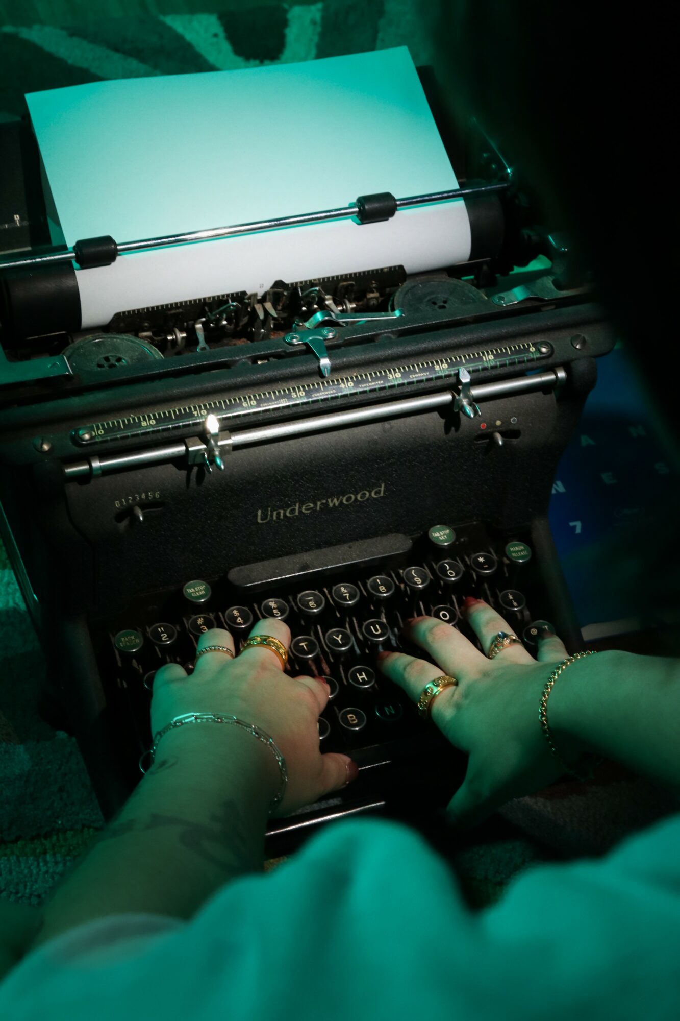 Person typing on a vintage typewriter with a sheet of paper inserted, illuminated by greenish light.