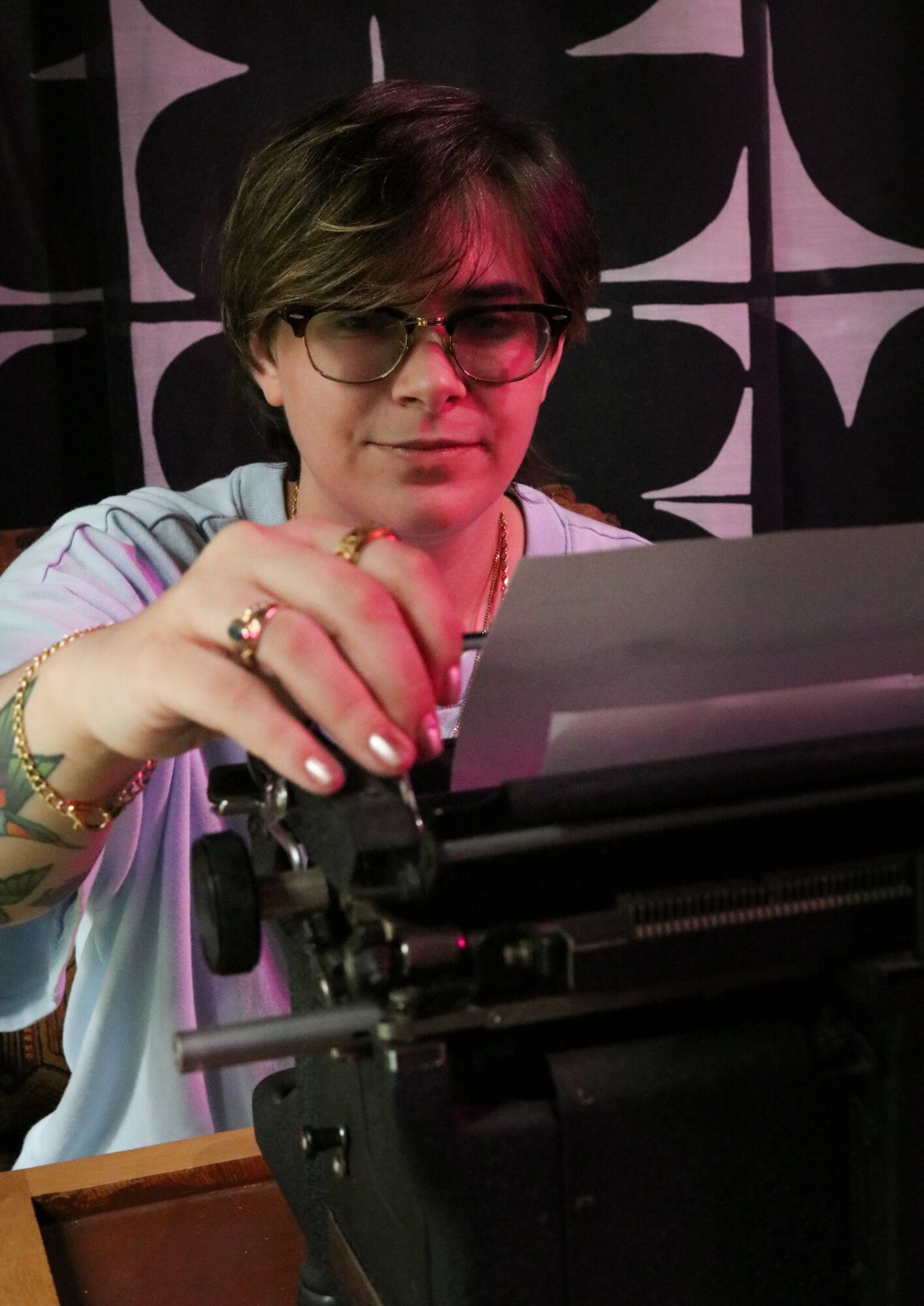 Person with short hair and glasses operating a typewriter, background with black and white geometric pattern