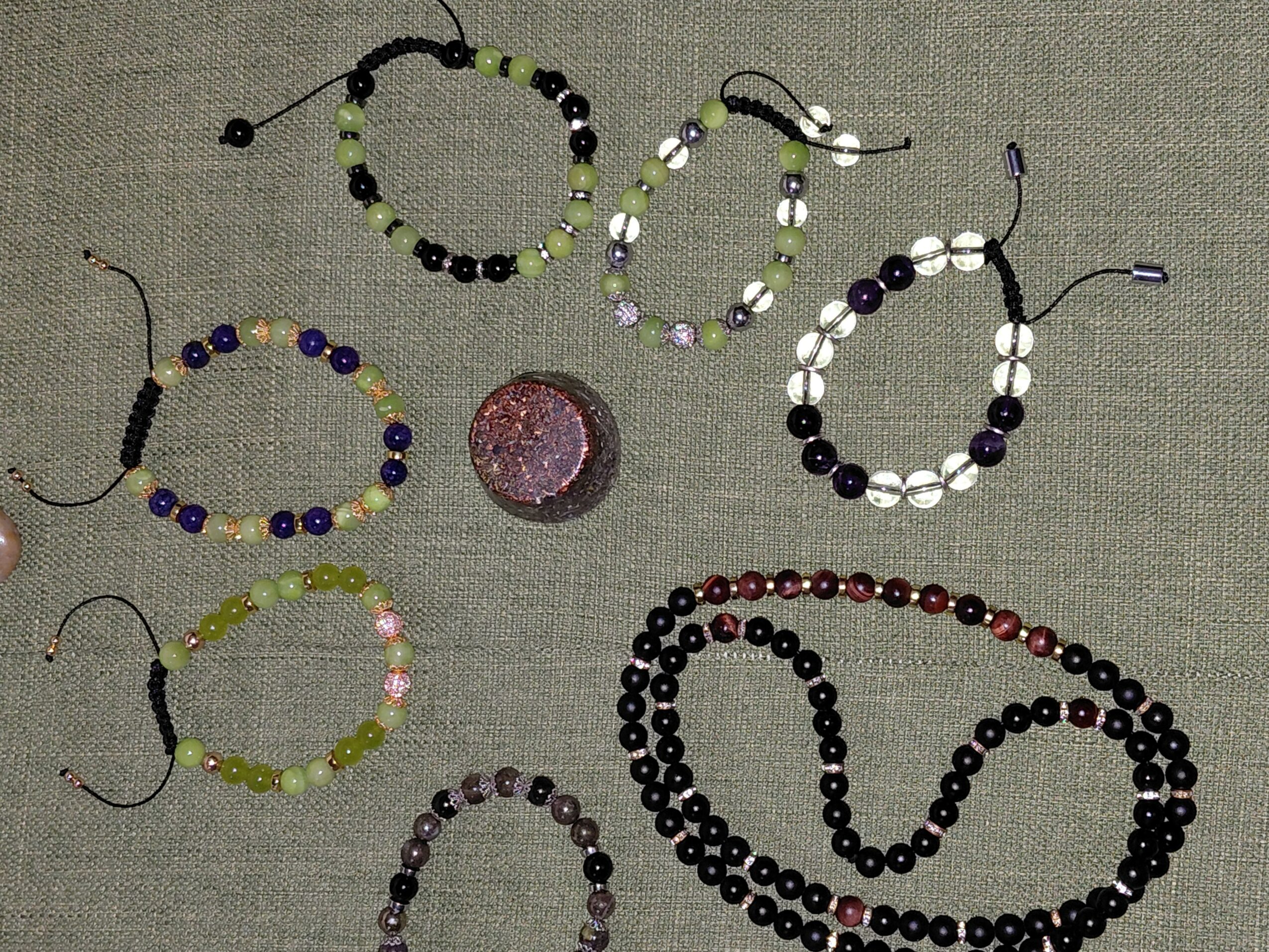 Beaded jewelry and a round object arranged on fabric surface, including bracelets and necklaces with various colors and patterns.