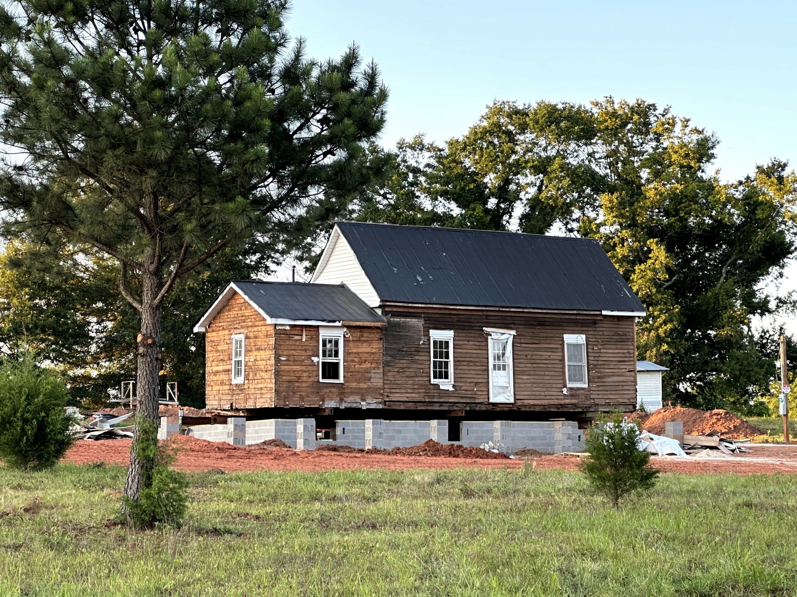 A wooden house under construction with a black roof, surrounded by trees and a grassy area.