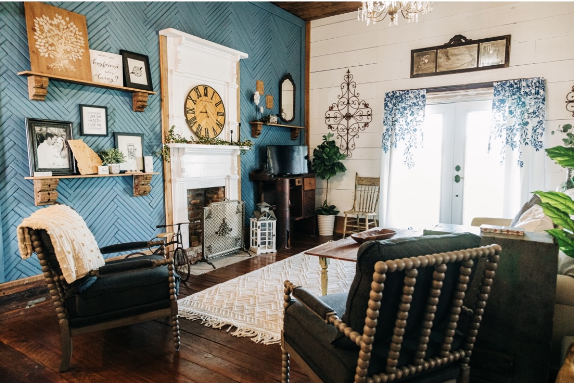 Living room with blue and white walls, fireplace, wooden furniture, and large window with curtains.
