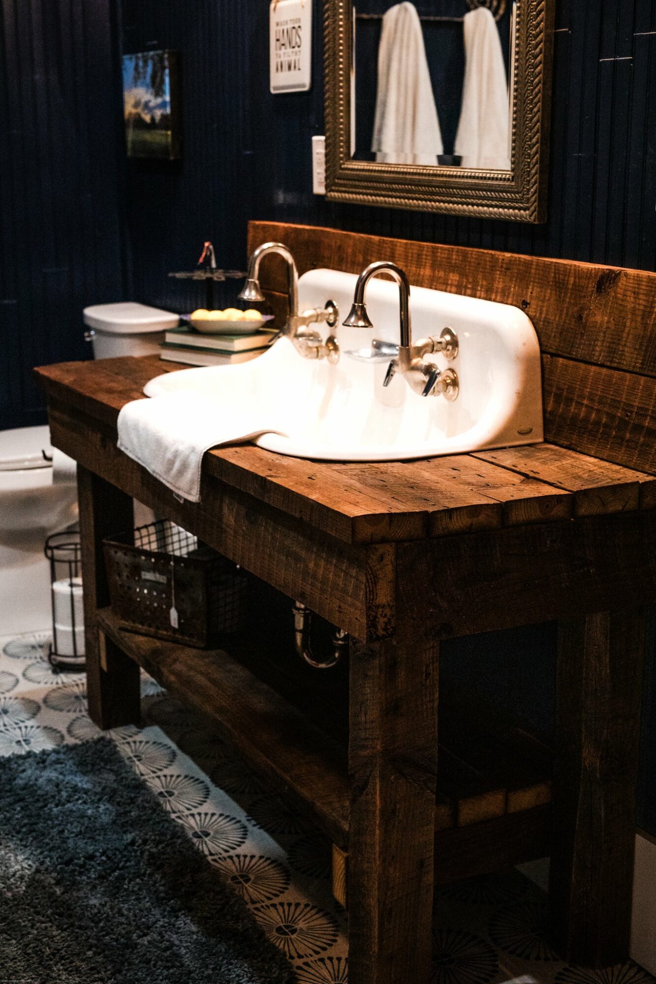 Bathroom sink with two faucets, mirror, and towels in a dark, rustic setting.