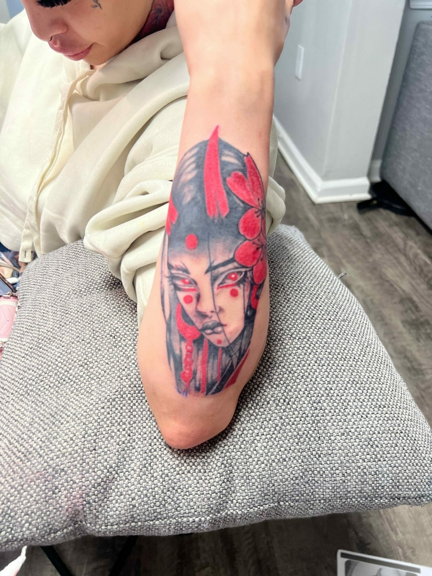 Tattooed arm resting on a gray cushion, with a colorful tattoo of a woman's face and red accents.