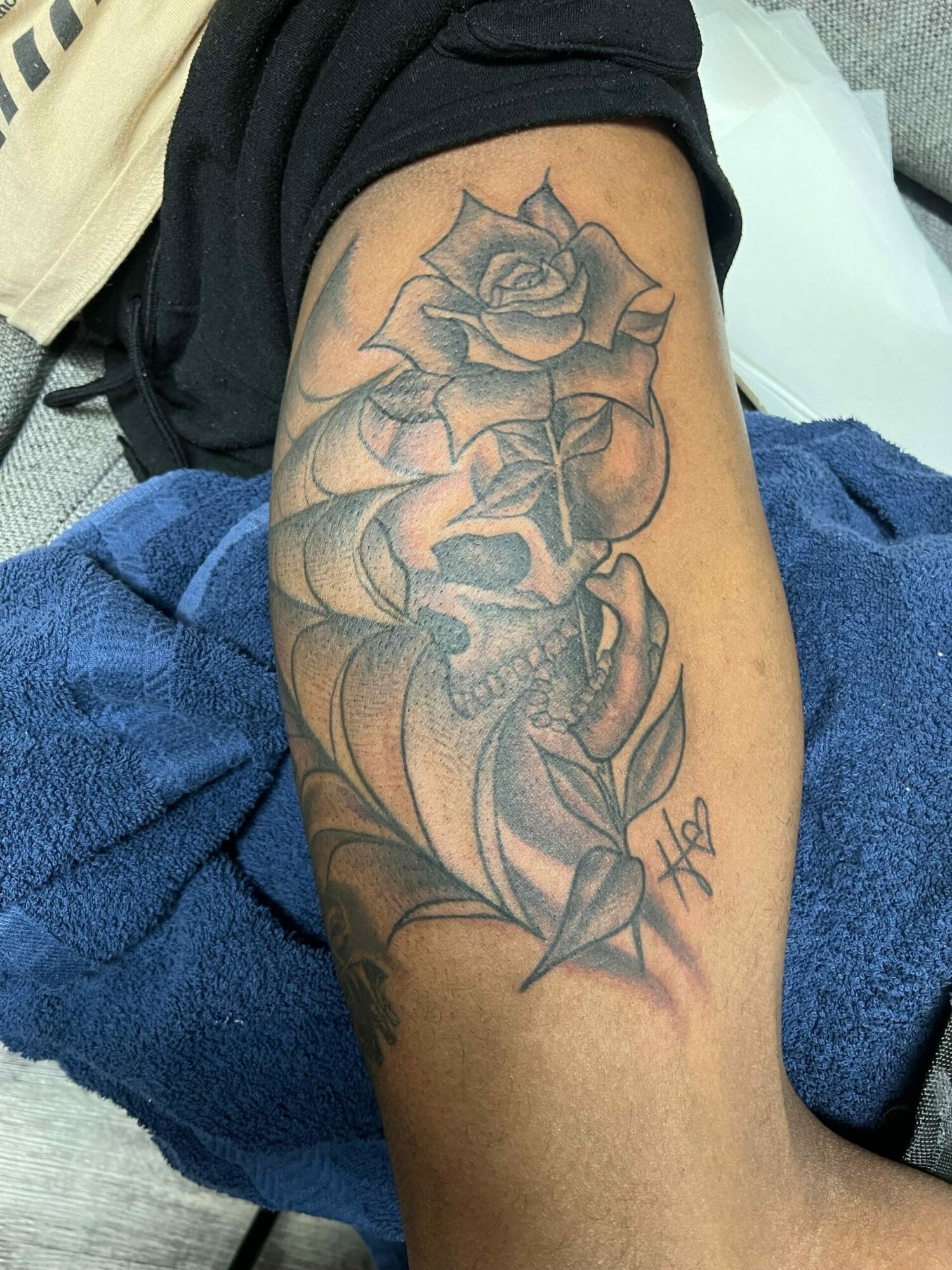 Tattoo of a skull surrounded by roses on person's arm, with detailed shading and line work.
