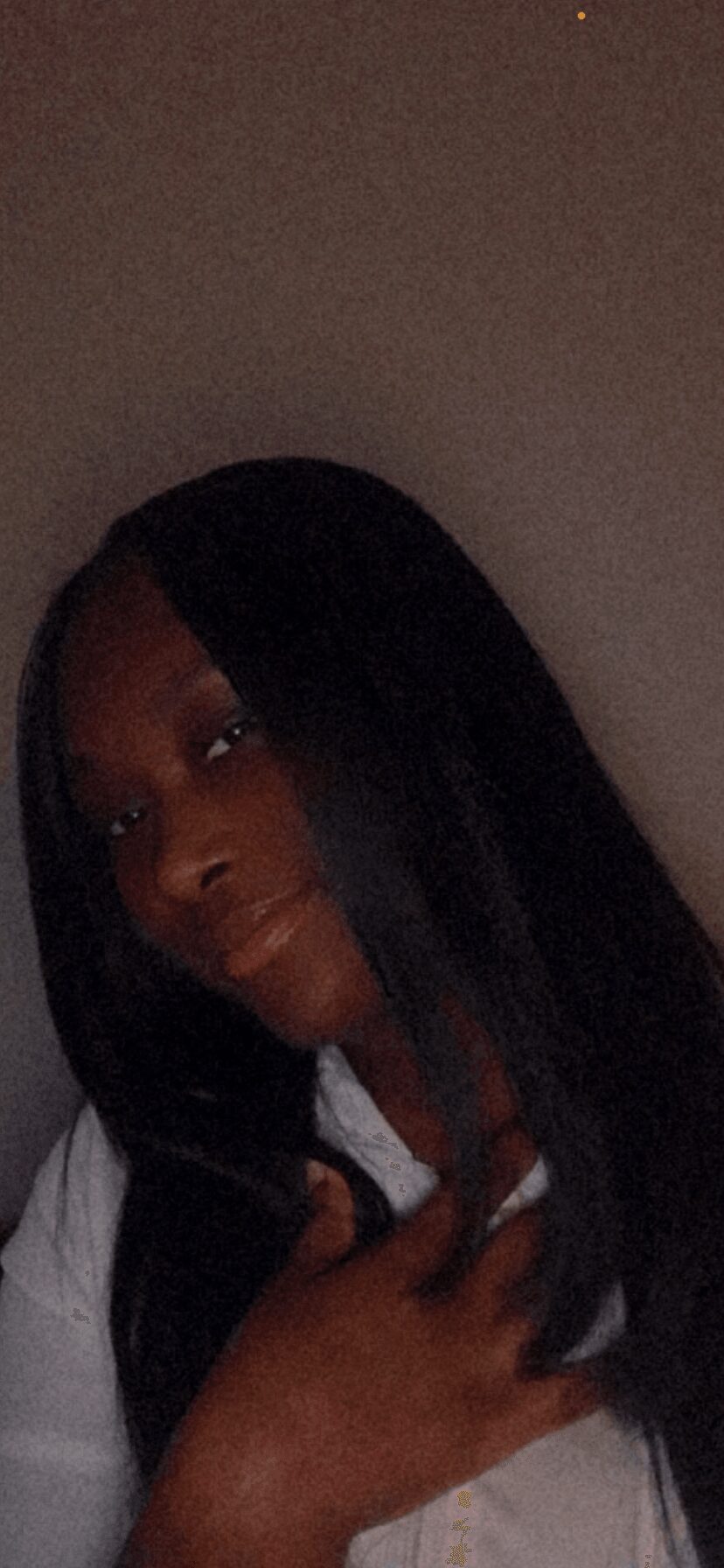 Person with long black hair making a peace sign gesture, dark background, partially visible face.