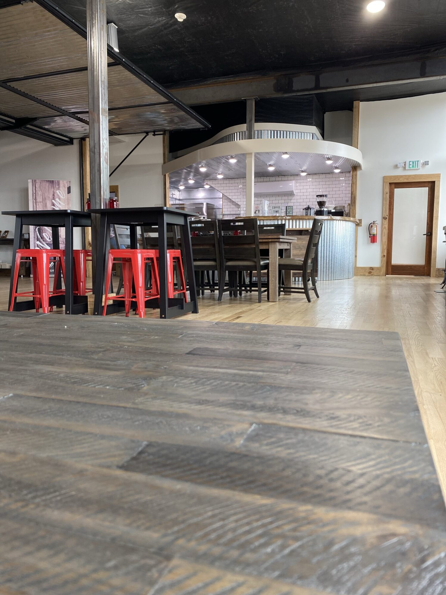 Interior of a restaurant with tables, chairs, and a bar area, with a wooden floor and ceiling, and a door on the right.