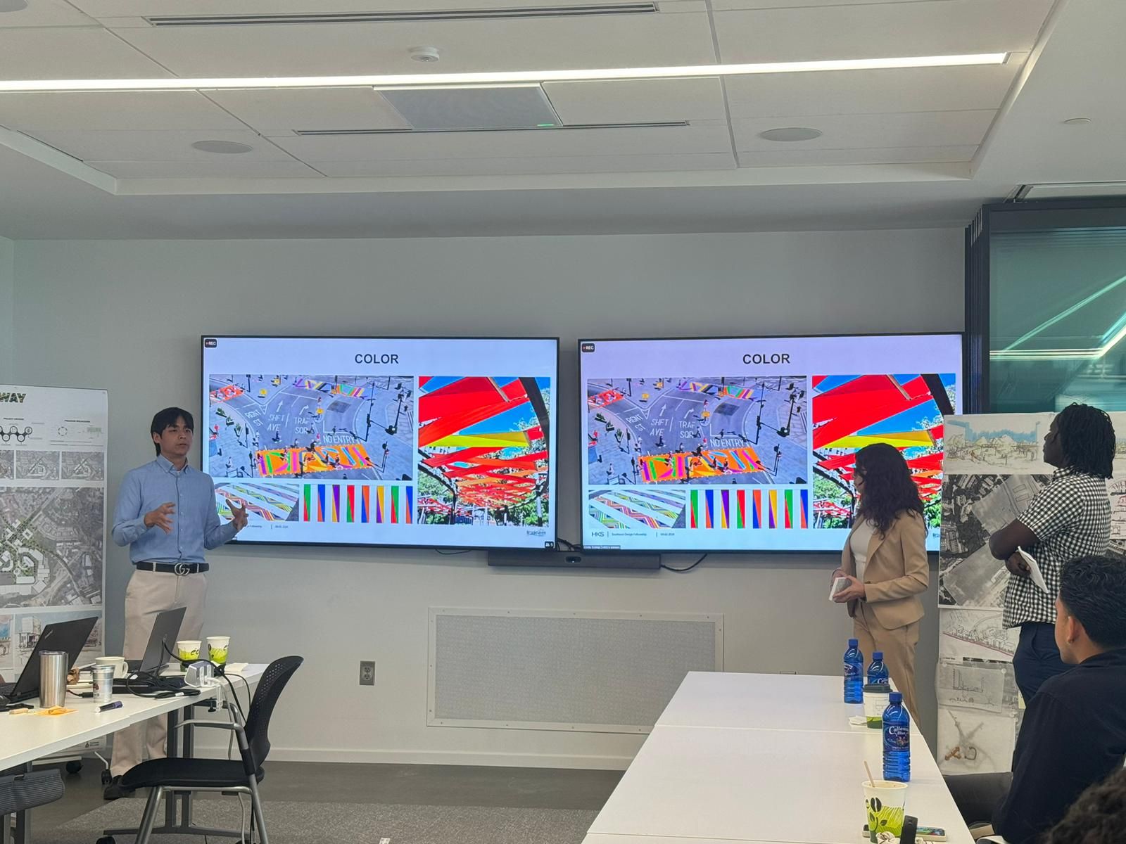 Two large screens display colorful abstract images in a modern conference room with people standing and sitting.