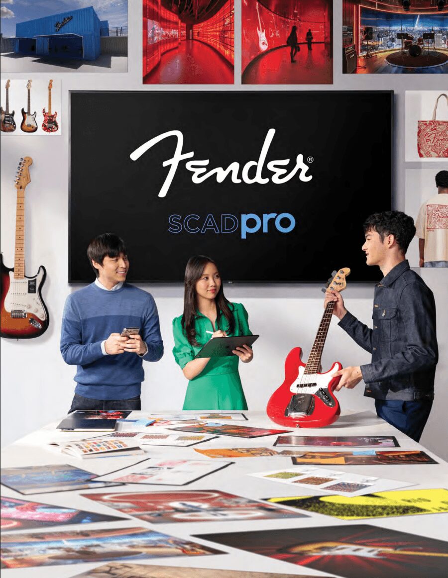 Three people in a room with a blackboard displaying 'Fender SCAD pro', surrounded by guitars and photos, discussing a red guitar.