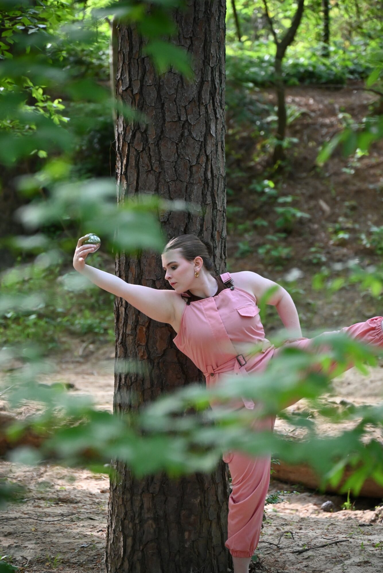 Woman in pink outfit stretching outdoors near a tree in a forest setting.