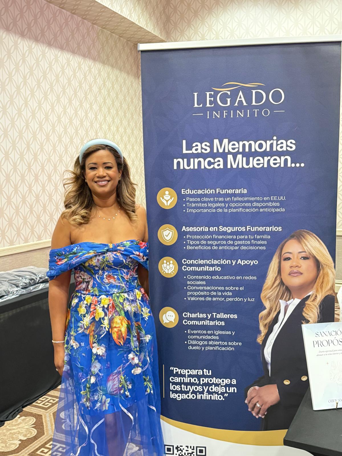 Woman in colorful dress standing next to a blue and white informational banner, smiling at the camera.