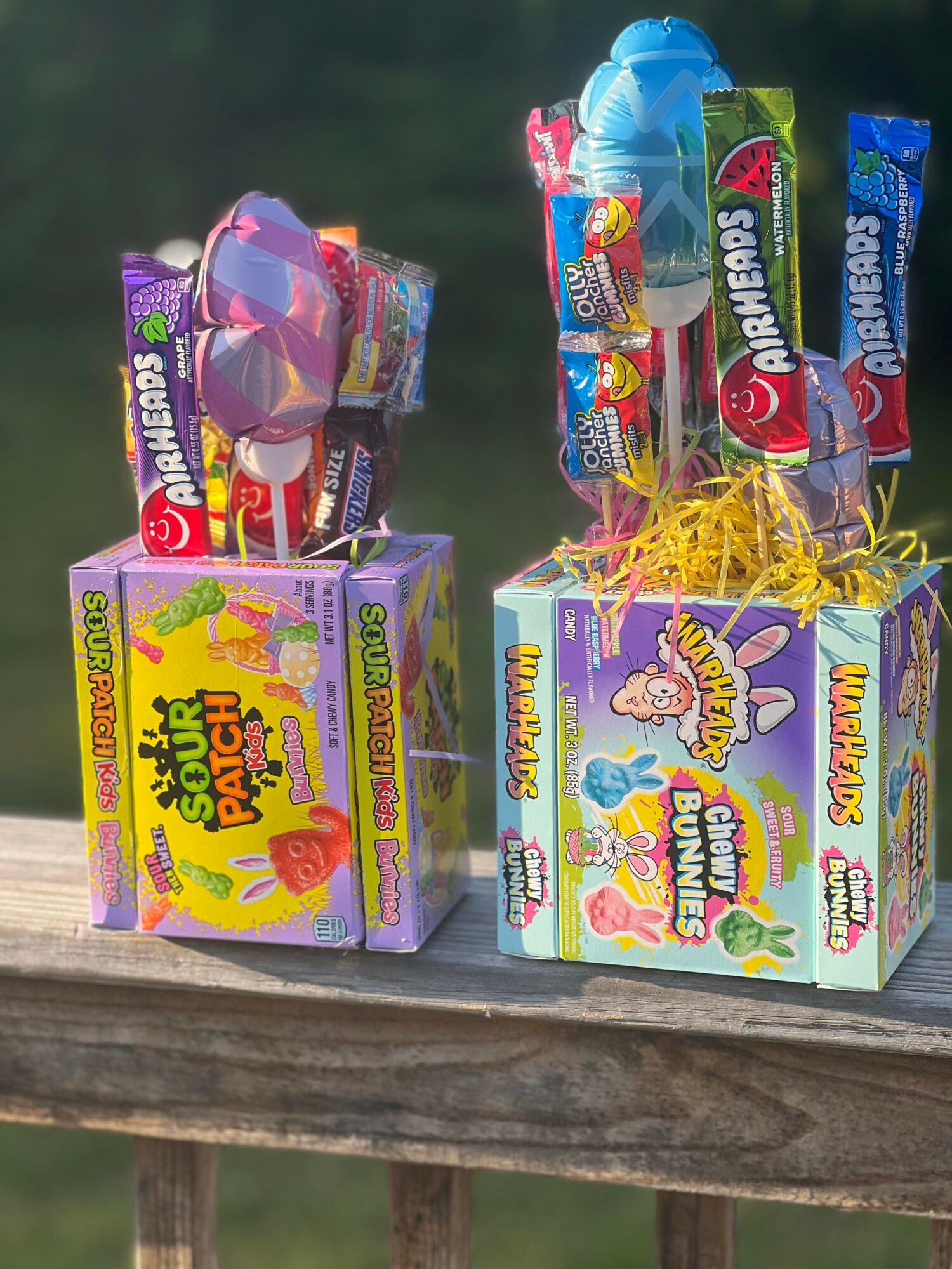 Two colorful toy packages with candy and toys, one purple and one blue, on a wooden surface outdoors.