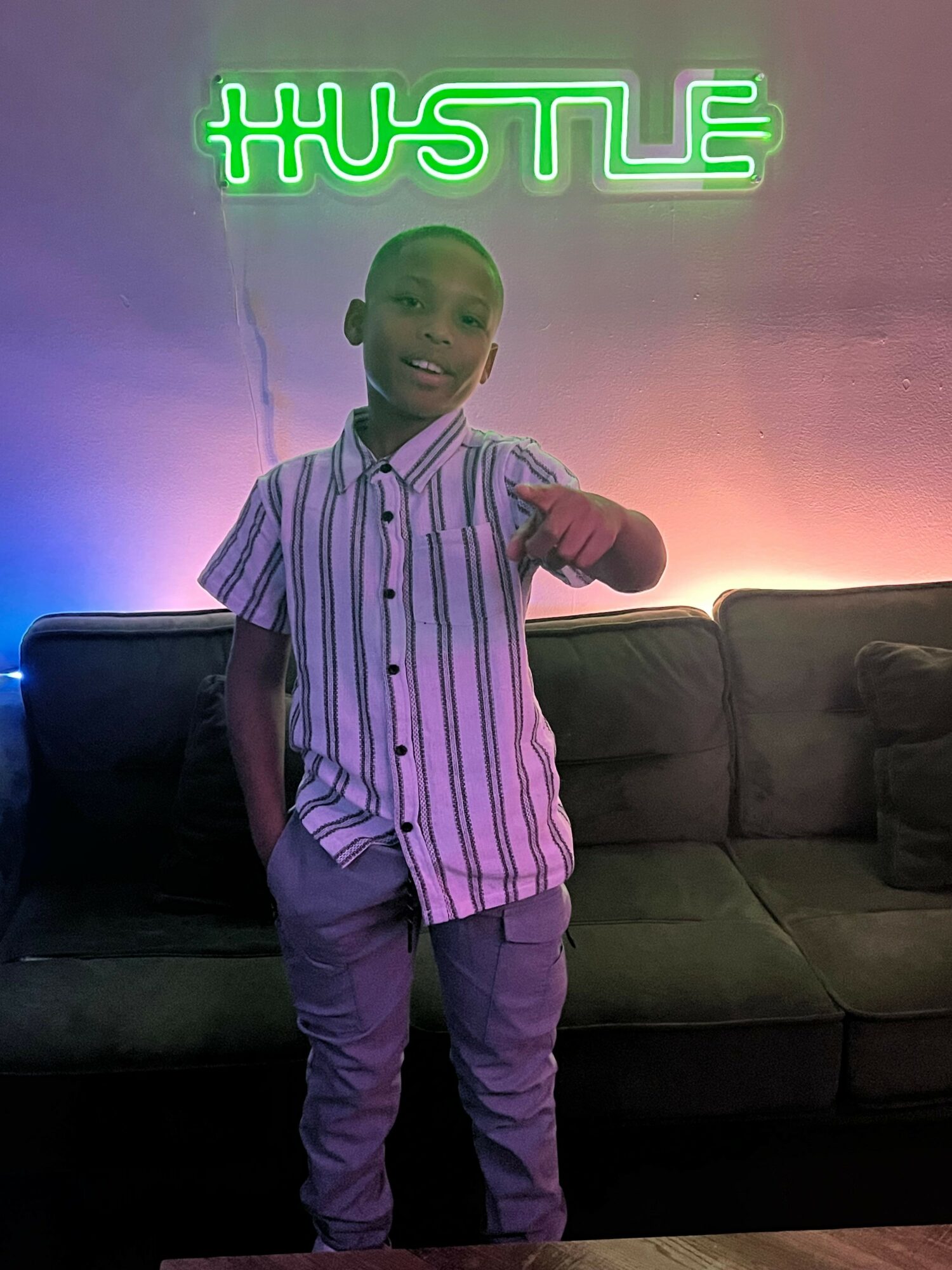 Person standing in front of a neon sign that reads #HUSTLE, with a sofa and colorful lighting in the background.