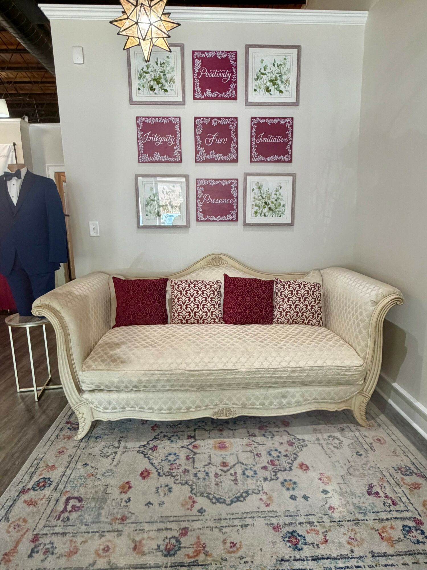 Cream-colored vintage sofa with red and patterned pillows, wall art, and a patterned rug in a cozy room.