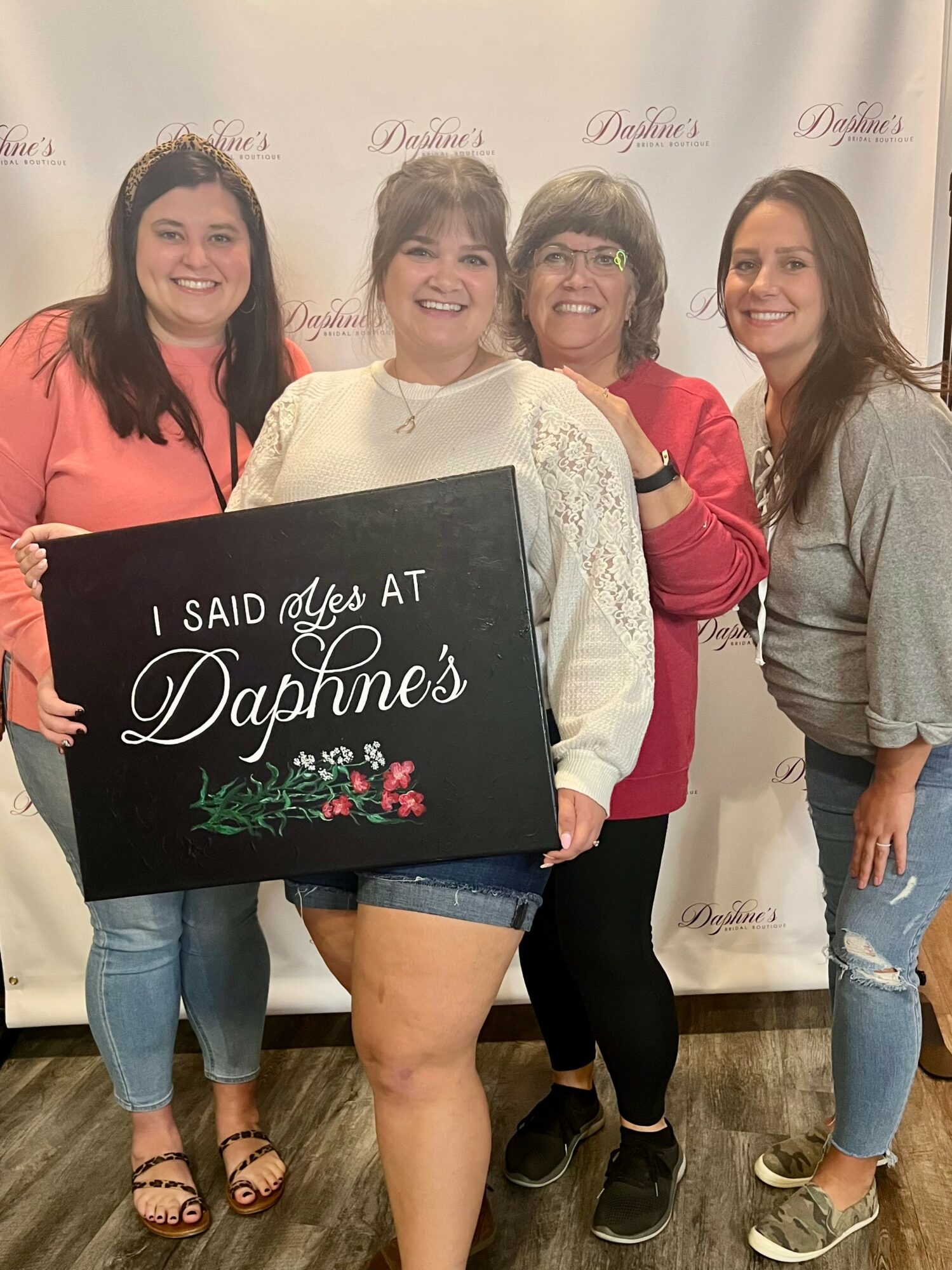 Four women smiling, holding a sign that says 