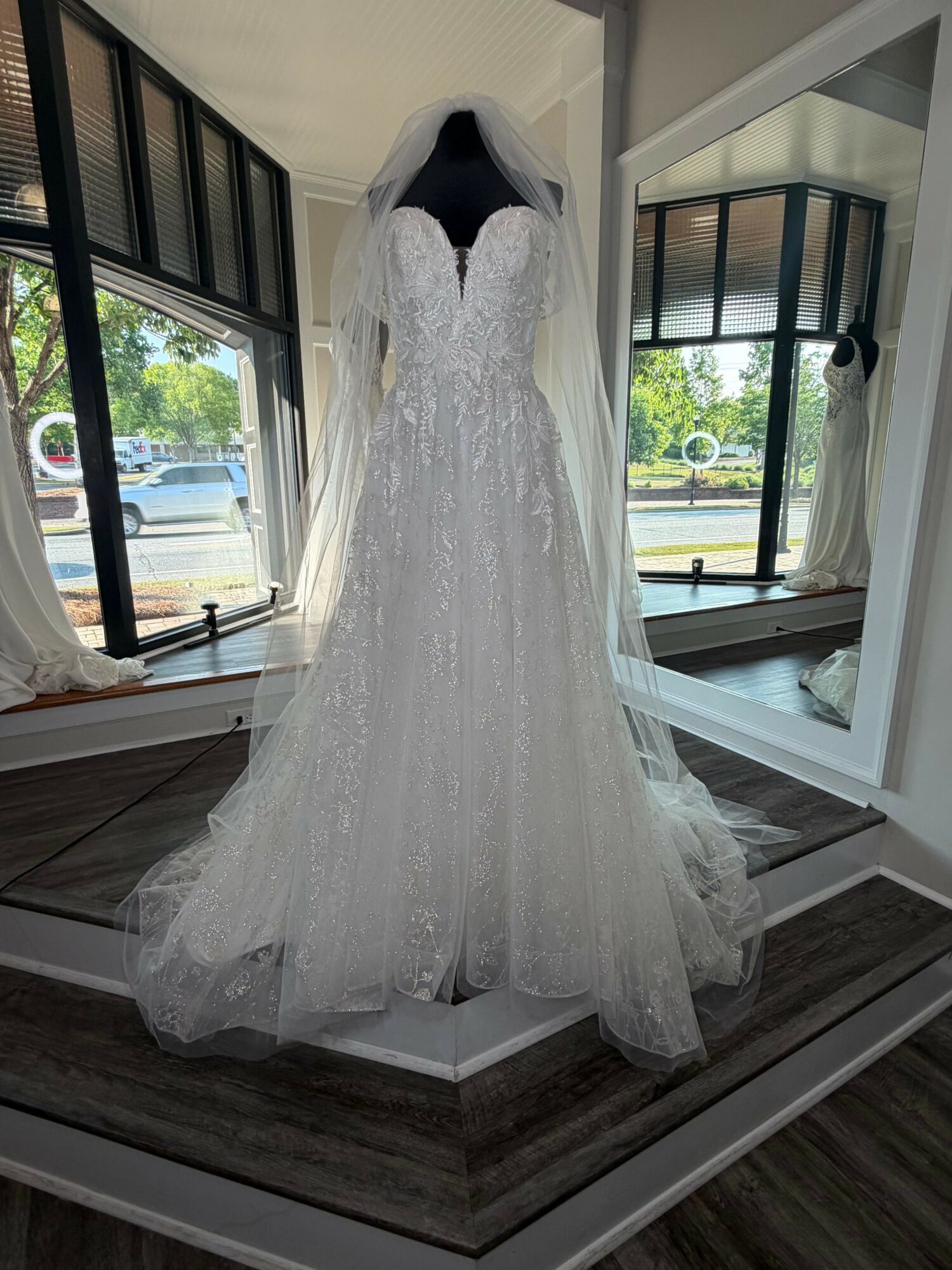 Wedding dress displayed on a mannequin in a room with large windows and a view outside.