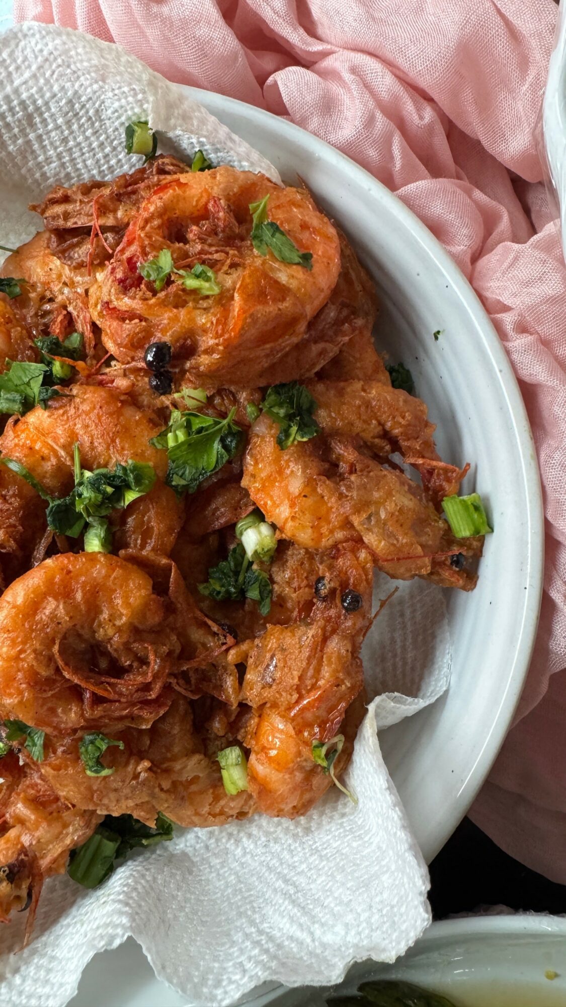 Plate of fried chicken pieces garnished with chopped green onions on a white dish, with a pink cloth nearby.