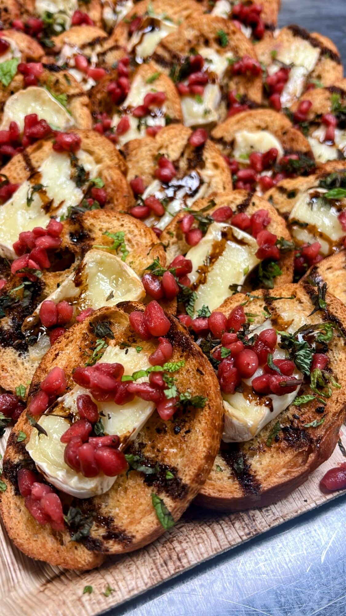 Close-up of bruschetta topped with cheese, pomegranate seeds, and herbs on a wooden board.