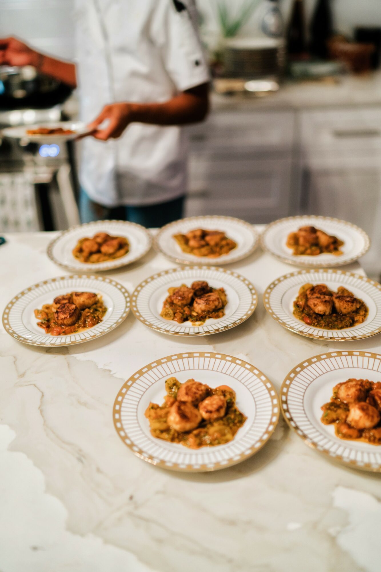 Several plates with fried food are arranged on a marble countertop in a kitchen, with a person in a white shirt in the background.
