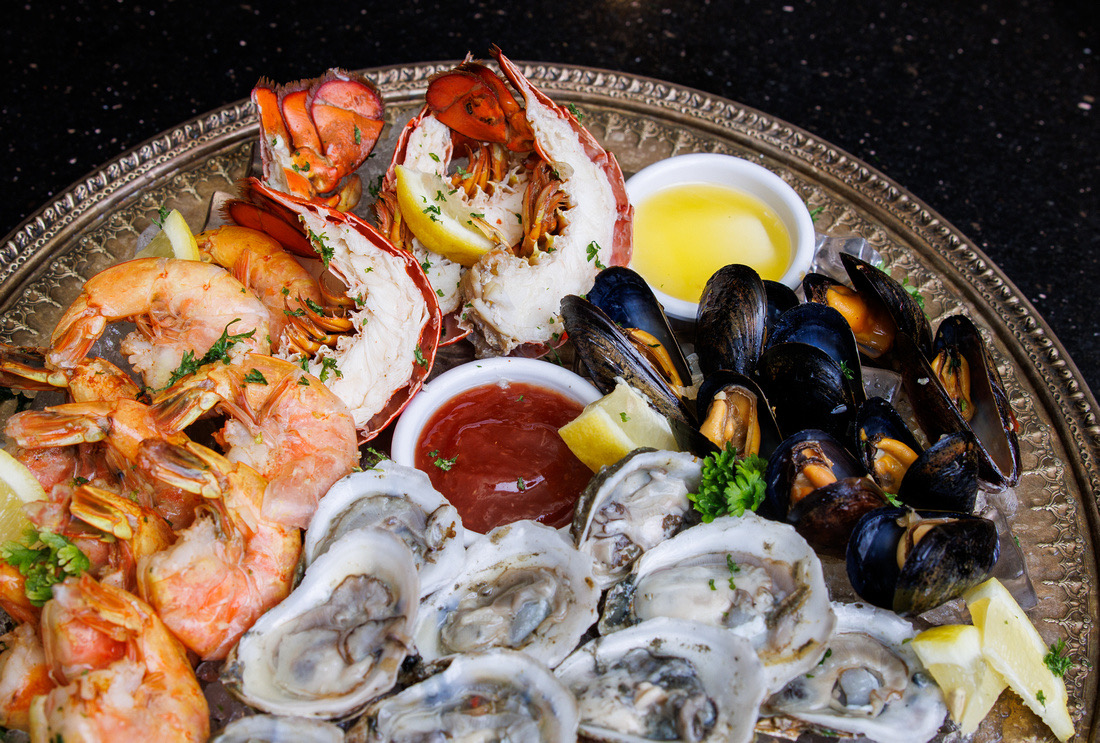 Seafood platter with lobster, shrimp, oysters, mussels, lemon wedges, and sauces on a decorative plate.