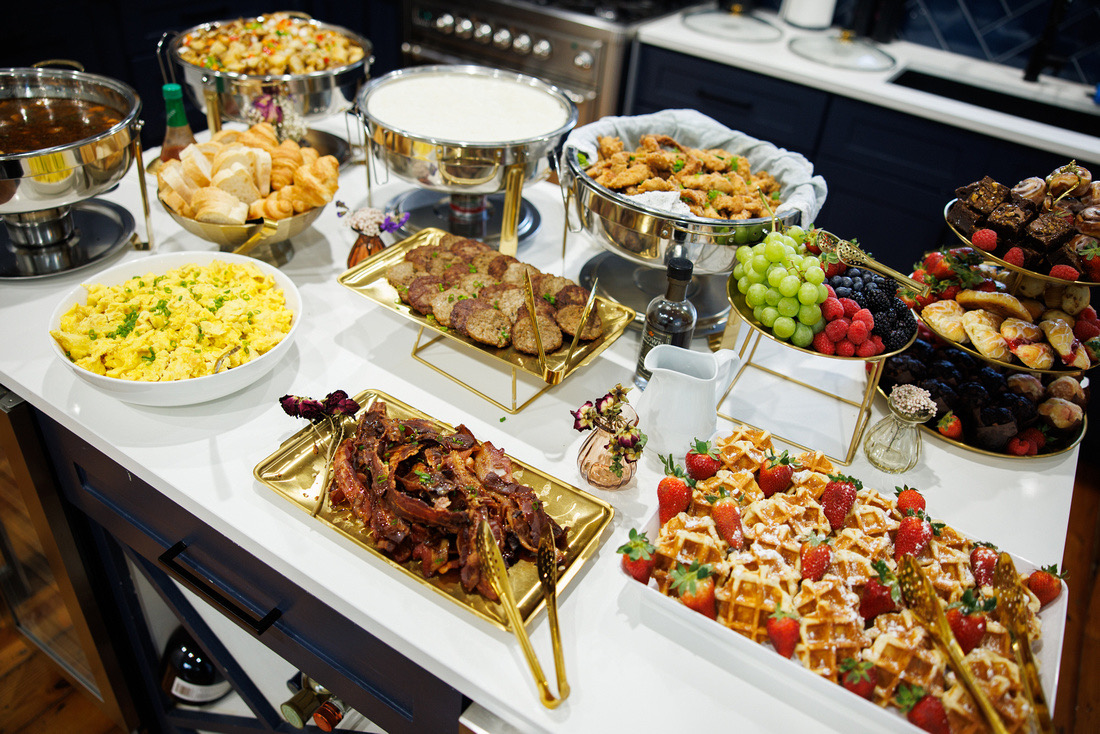 Table with various dishes including salads, meats, fruits, and desserts on a kitchen counter.