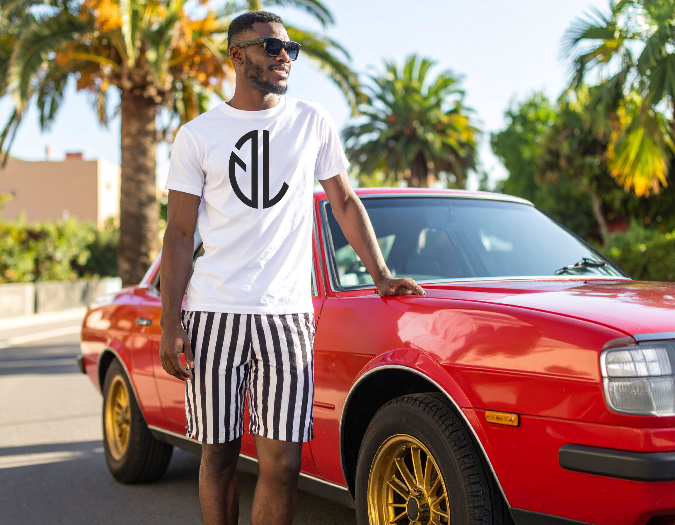 Man in sunglasses wearing a white t-shirt with a black logo, striped shorts, standing next to a red car with gold wheels, palm trees in background.