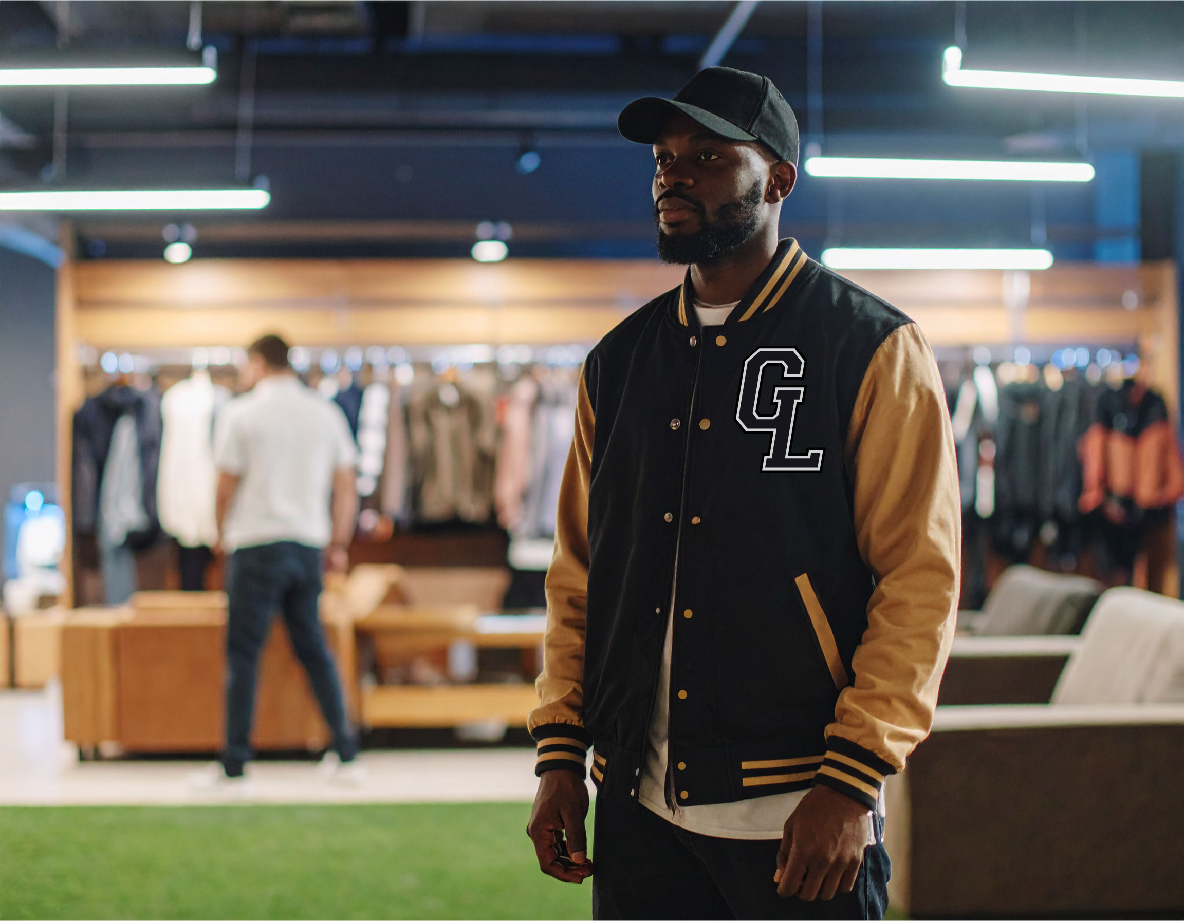 Man wearing a black and tan varsity jacket and cap stands in a clothing store with people shopping in the background.