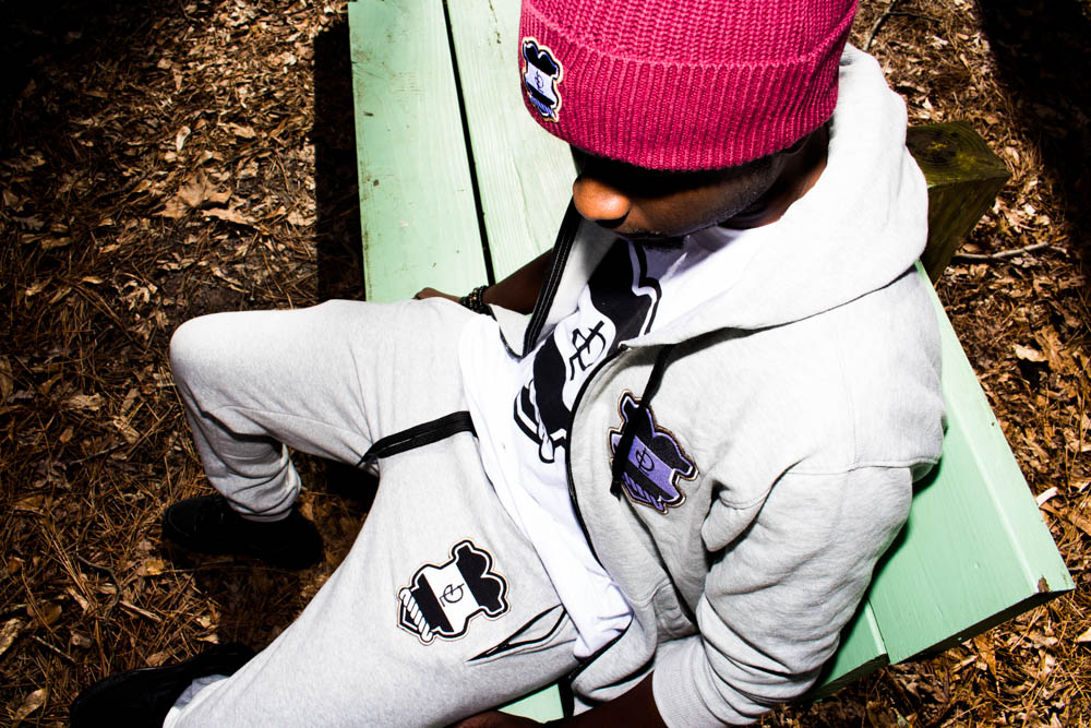 Child sitting on a green bench outdoors, wearing a pink hat and white hoodie, looking down, surrounded by leaves.