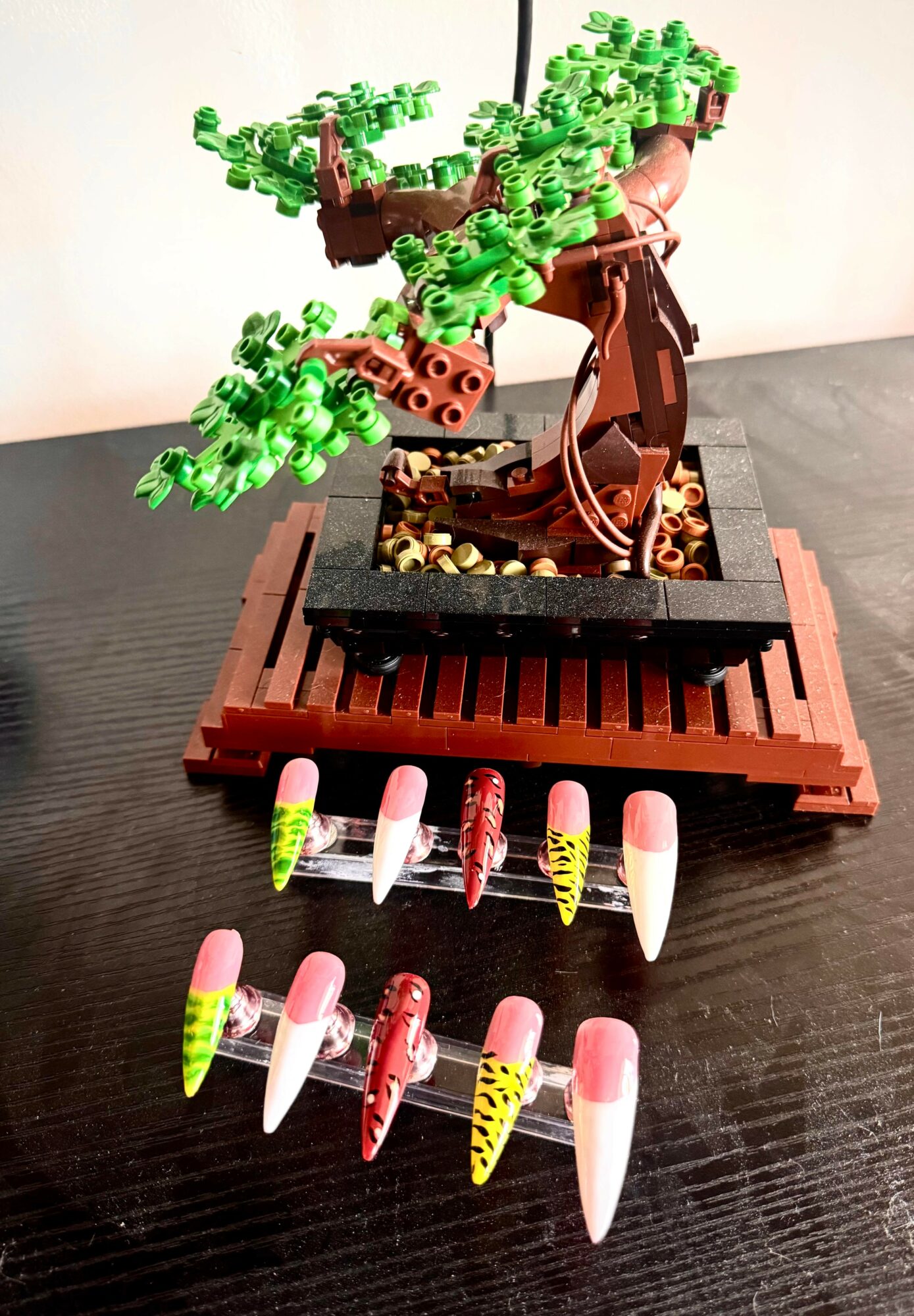 Lego bonsai tree with a wooden stand and decorative nails on a dark surface.