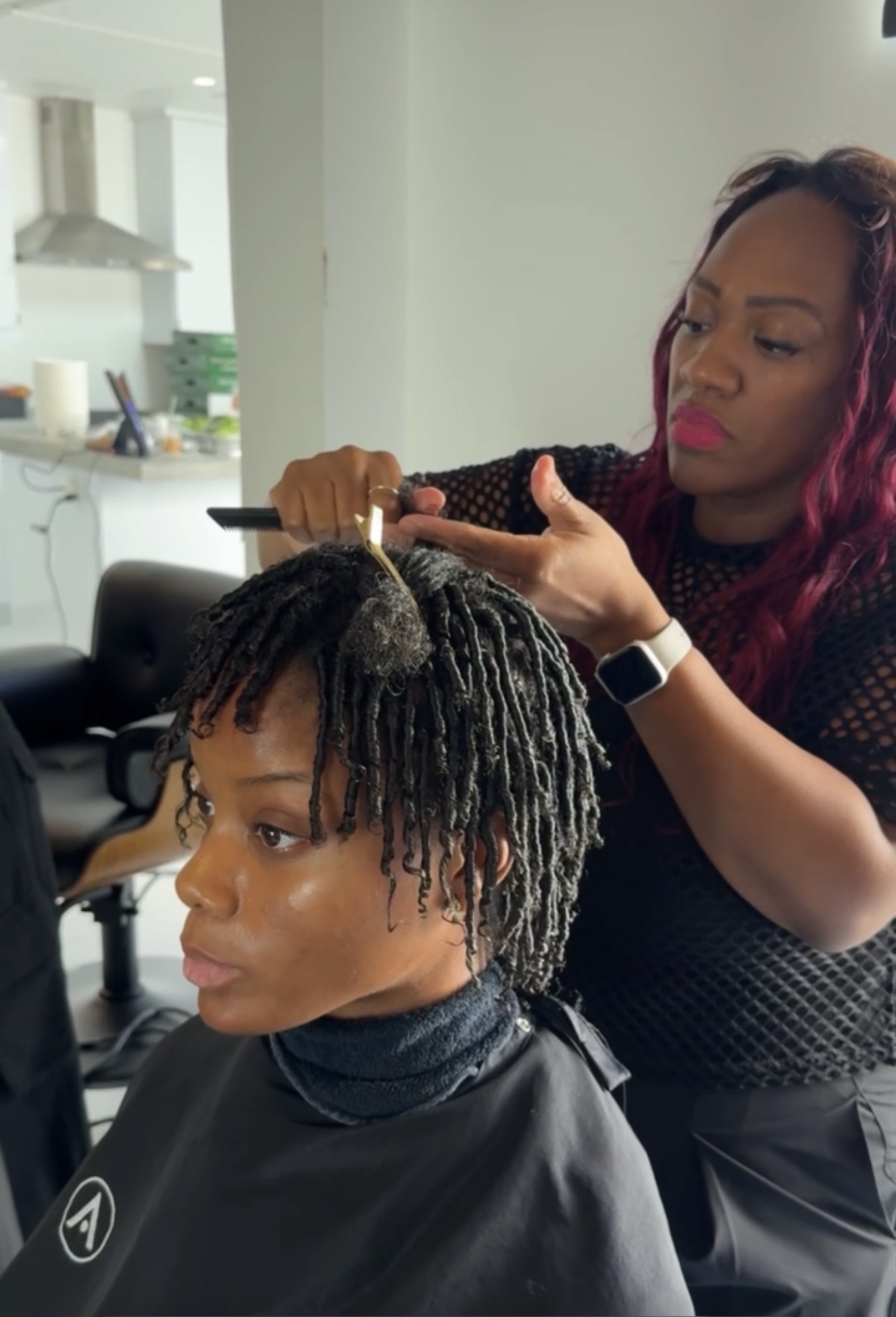 Woman getting her hair styled with a tool, in a salon setting, with a stylist working on her hair.