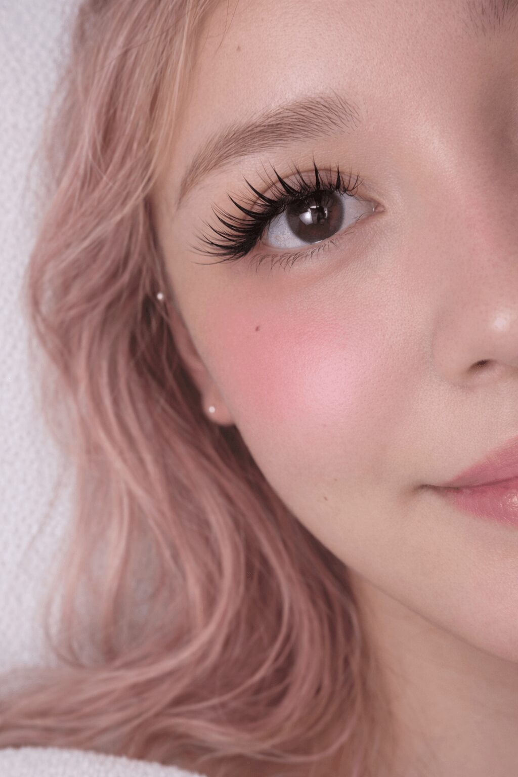 Close-up of a young woman's face showing her eye, eyebrow, and part of her cheek with pink hair.