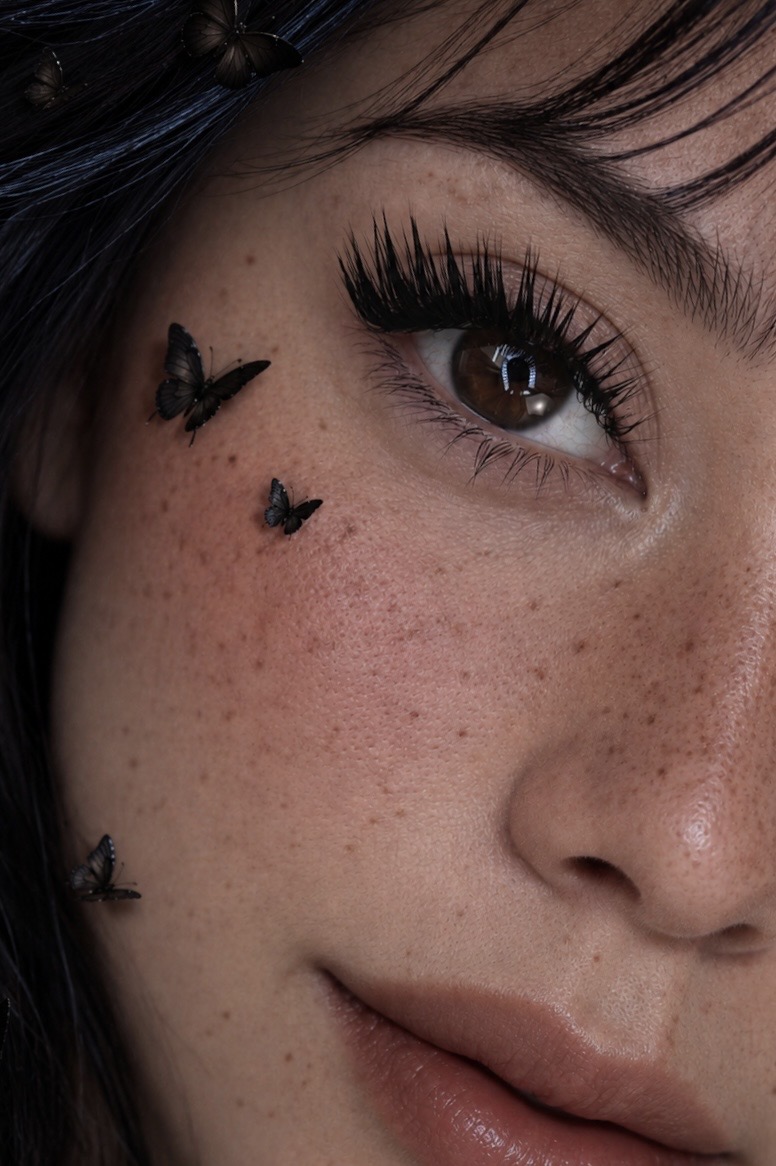 Close-up of a woman's face showing eye makeup, freckles, and butterfly face art.