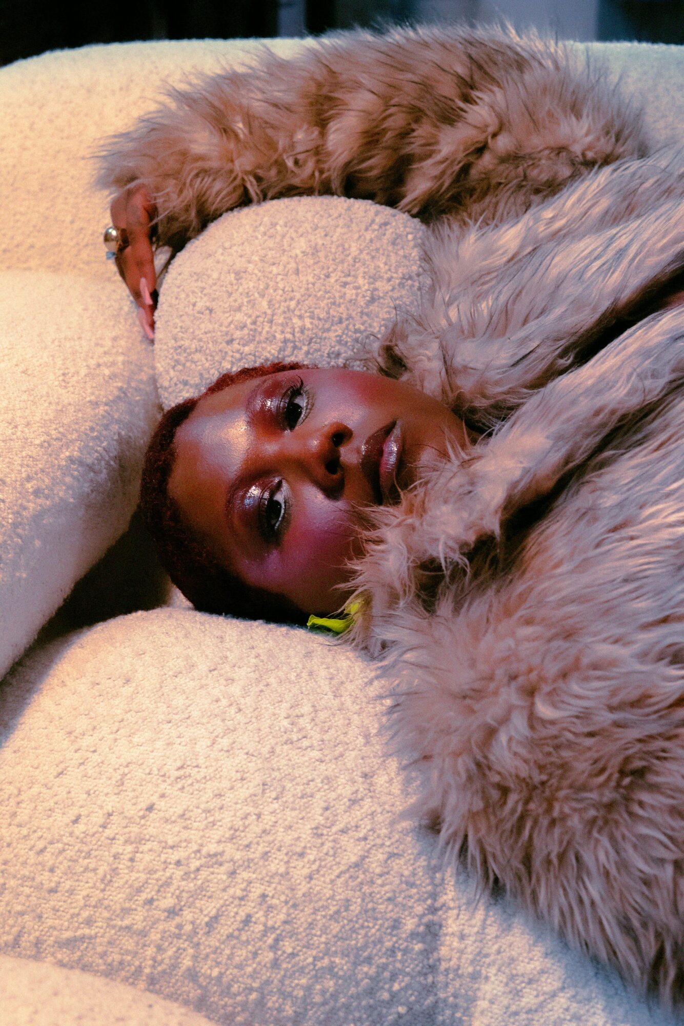 Person lying on a soft surface with a furry blanket, looking at the camera, surrounded by plush textures.