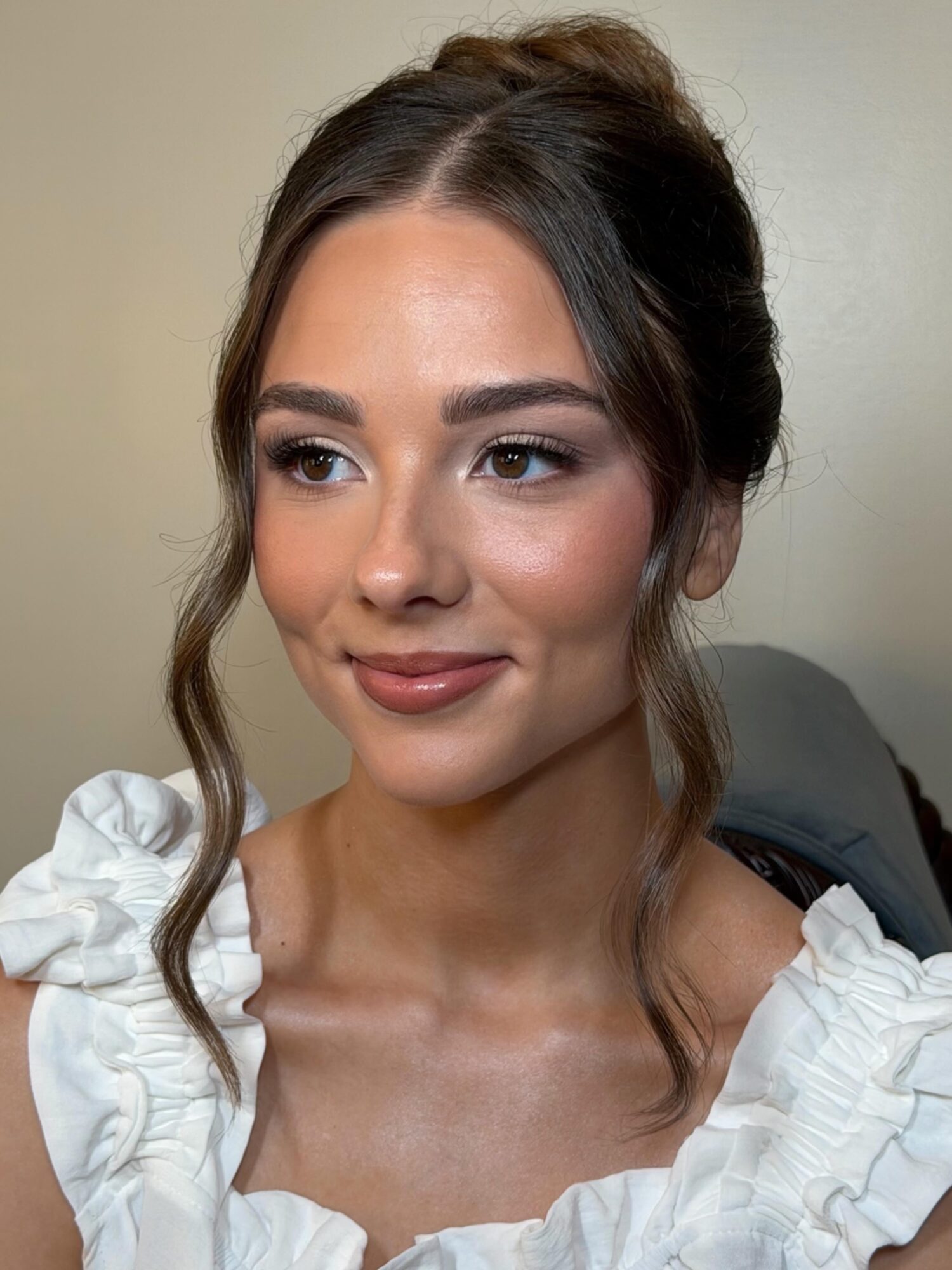 Young woman with styled hair, wearing a white ruffled top, smiling softly, facing slightly to the right.