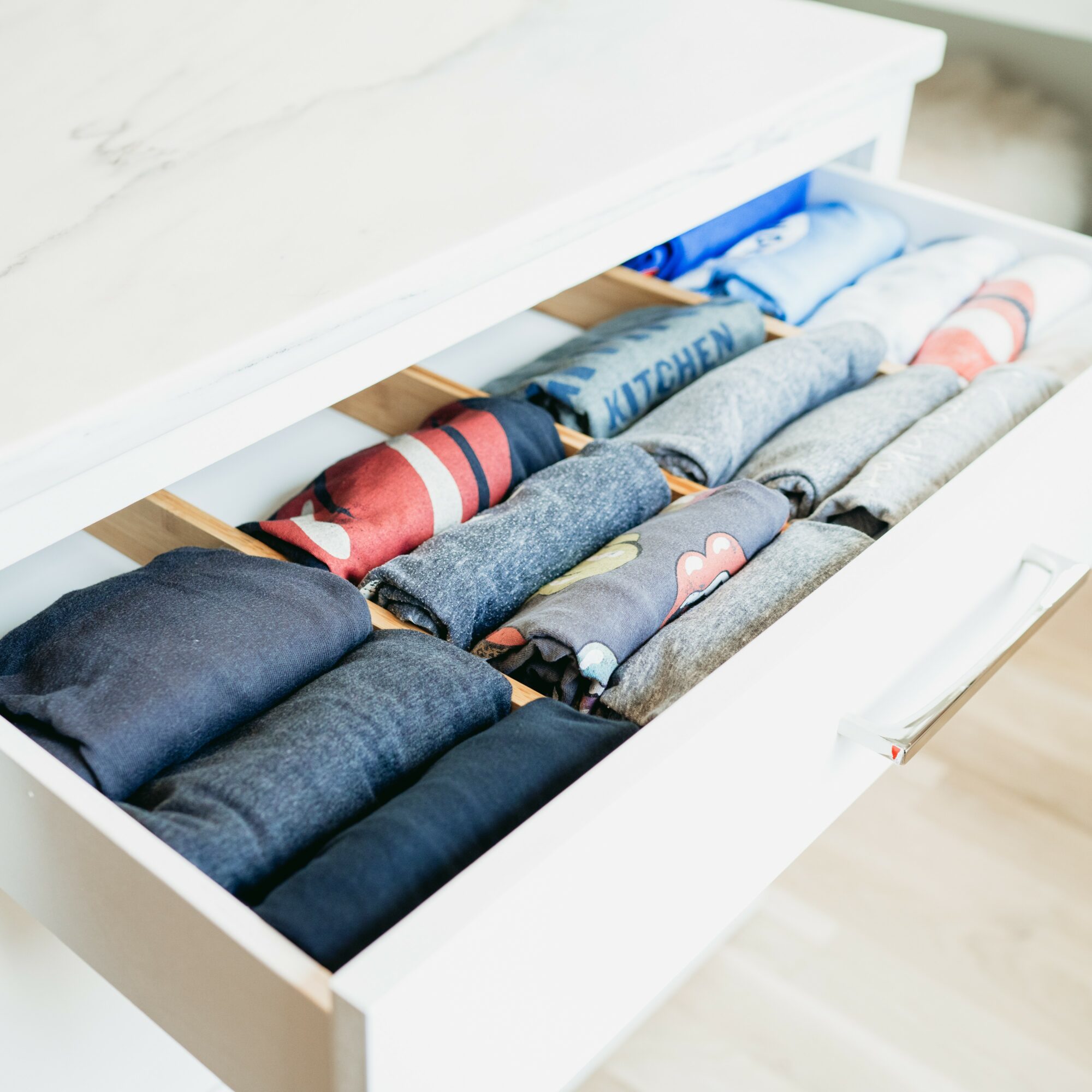 Drawer with neatly folded colorful and gray underwear, organized in rows inside a white drawer.