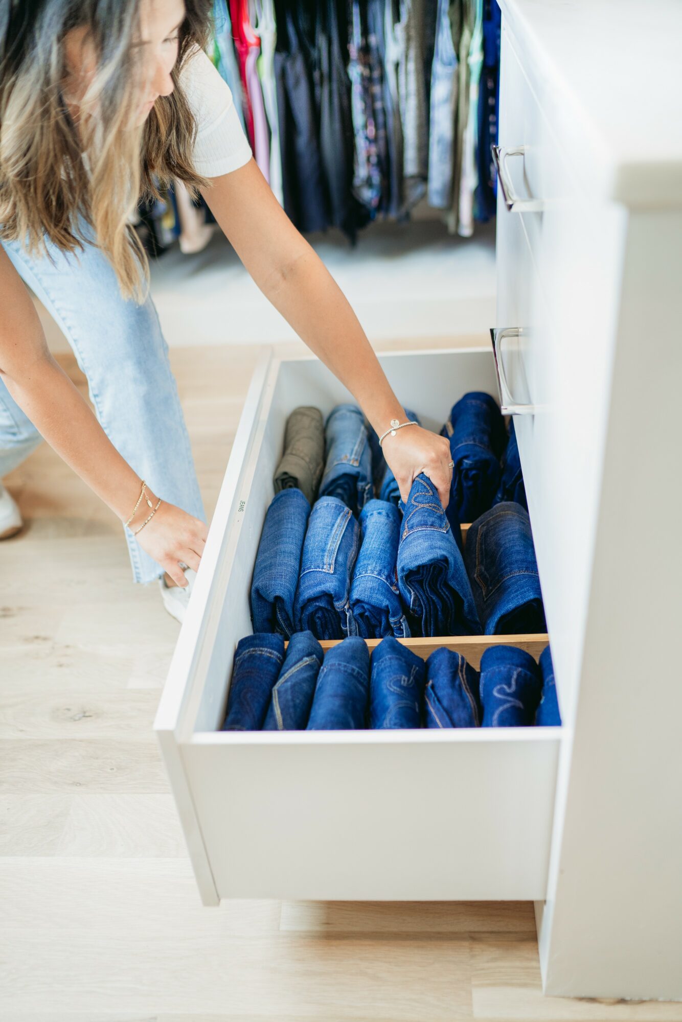 Person reaching into a drawer filled with blue and gray shoes, with clothing hanging in the background.
