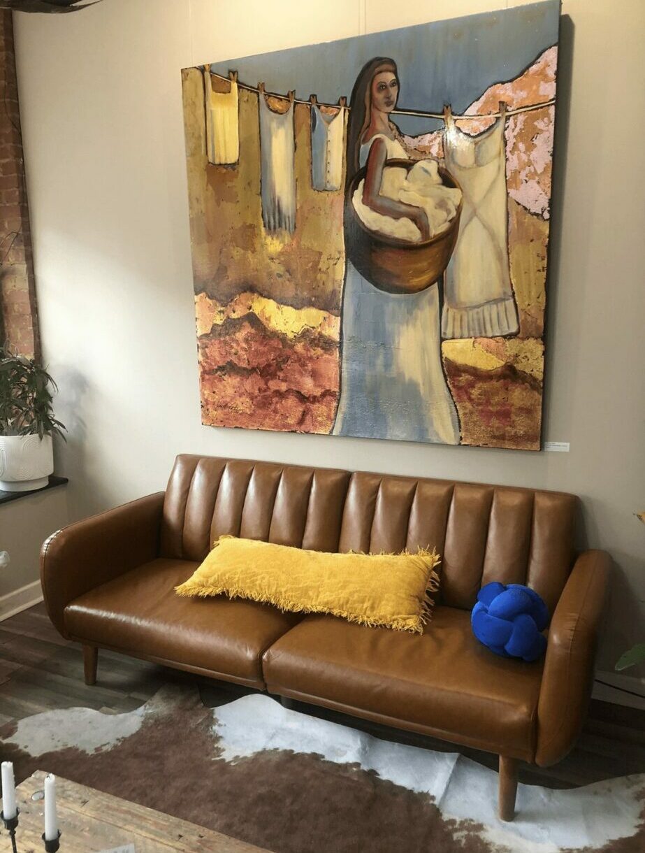 Living room with a brown sofa, yellow and blue pillows, and a large painting of a woman on the wall.